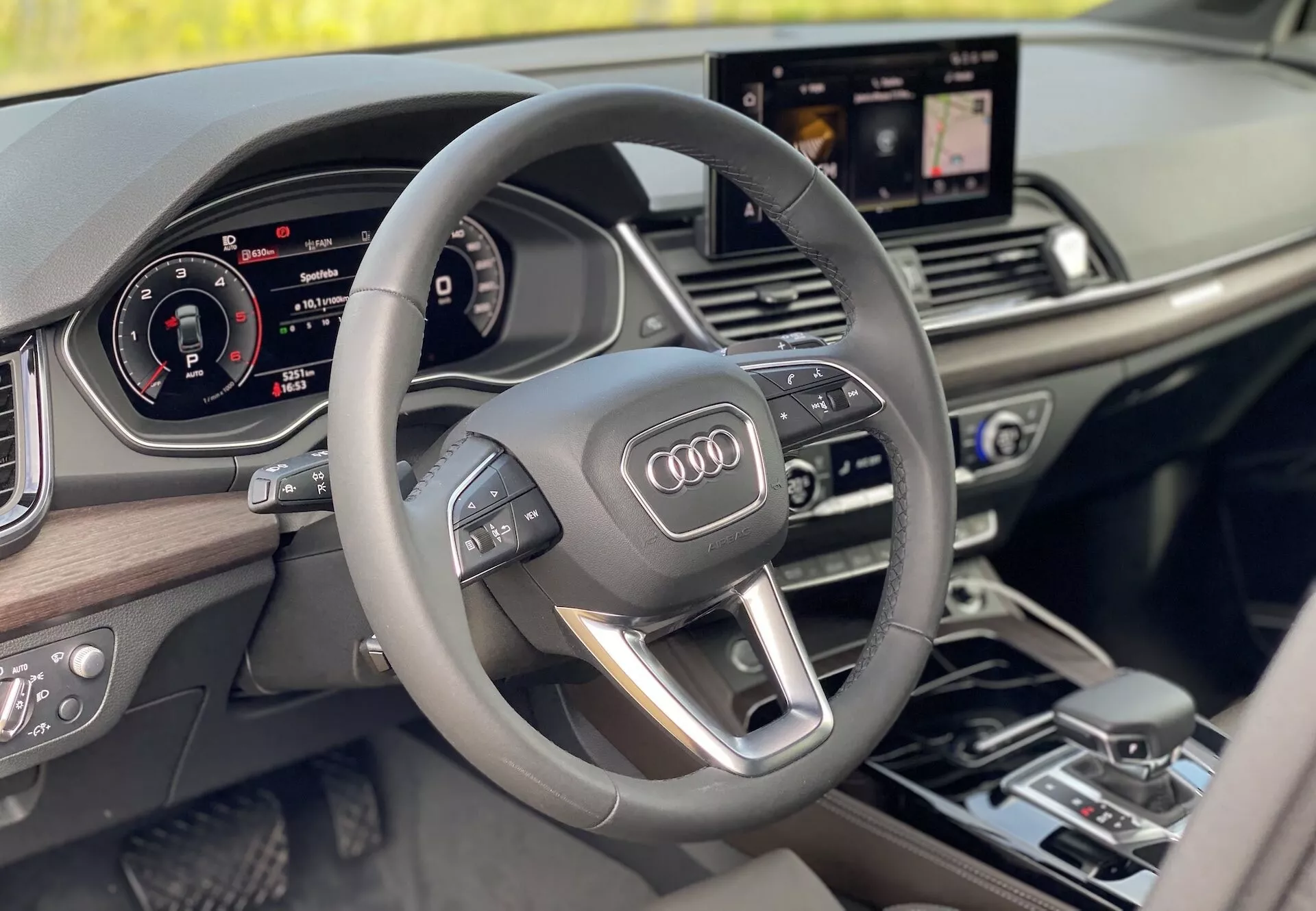 Intérieur de luxe de l'Audi Q5 2020 Sportback vu de la perspective du conducteur, avec un volant multifonction moderne à trois branches avec commandes intégrées, un tableau de bord entièrement numérique et un écran d'infodivertissement central affichant la navigation. Le design intérieur présente des accents en bois, soulignant un sentiment de luxe et de modernité.