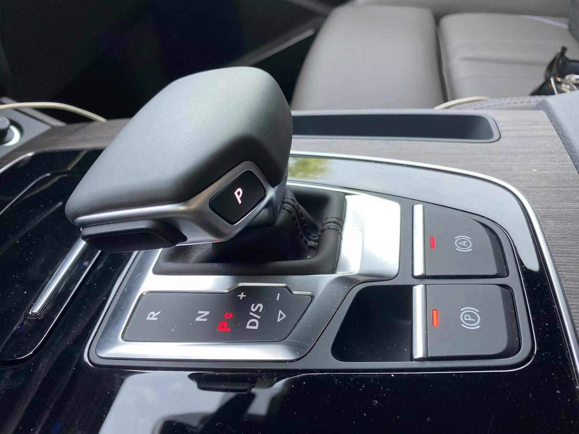 Gros plan du sélecteur de vitesse automatique de l'Audi Q5 2020 Sportback dans la console centrale, avec une conception shift-by-wire en position 'P' (Parc), des options 'R' (Marche arrière), 'N' (Neutre) et 'D/S' (mode de conduite/sport), ainsi que des symboles '+' et '-' pour le changement manuel, un bouton 'Auto Hold' et un frein de stationnement électronique. Le sélecteur est entouré d'une finition en noir piano et d'accents chromés, indiquant un intérieur luxueux et technologiquement avancé.