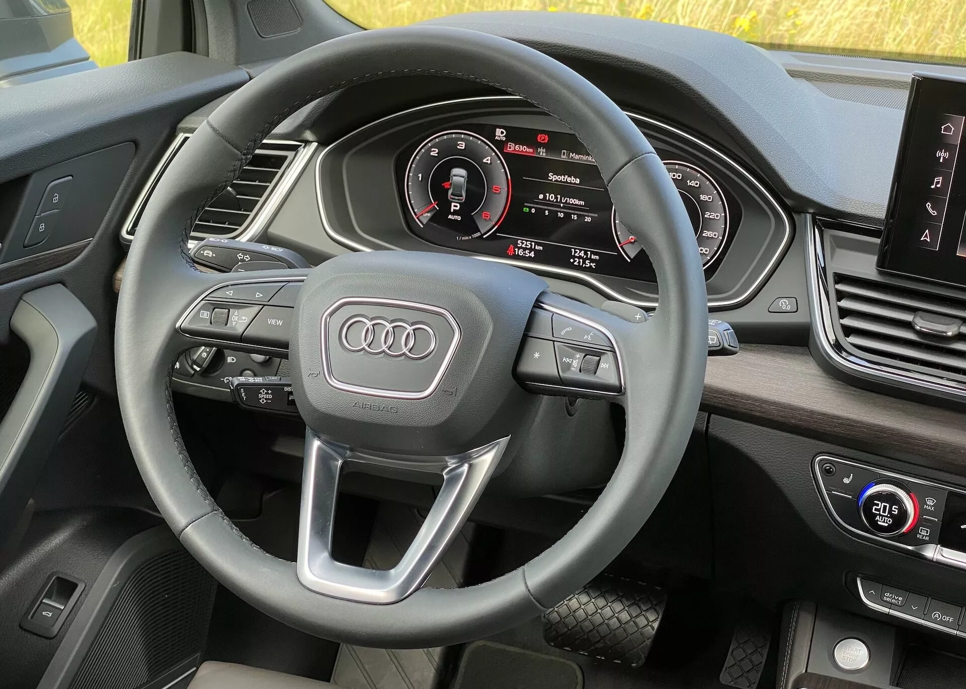 Intérieur de l'Audi Q5 Sportback 2020 vu du côté conducteur, montrant le volant avec commandes multifonctions et l'emblème Audi, tableau de bord numérique avec compteur de vitesse, compte-tours, affichage central d'infodivertissement et commandes de climatisation, avec matériaux de haute qualité.