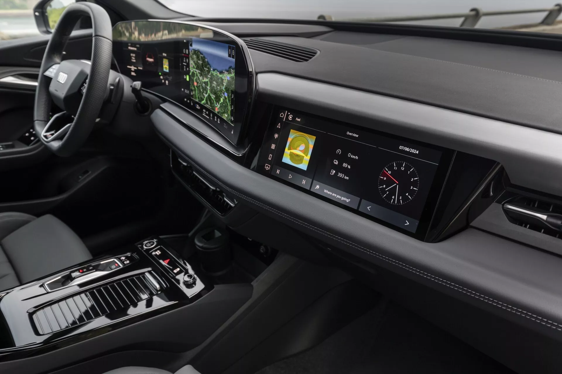 Vue intérieure de l'Audi Q6 e-tron 2024, centrée sur le tableau de bord et la console centrale depuis un angle légèrement surélevé. À gauche, on aperçoit le volant, indiquant une configuration de conduite à gauche, tandis que la console centrale comprend un levier de vitesses, divers contrôles et un grand écran tactile. Le tableau de bord numérique affiche les métriques de conduite. Le tableau de bord élégant s'étend horizontalement avec des bouches d'aération et un autre élément de design à droite. La technologie avancée est évidente grâce à l'écran tactile central affichant des informations de navigation et multimédias, un affichage tête haute visible au-dessus du volant et des boutons sensibles au toucher pour le contrôle climatique. Le design met en avant le minimalisme et les matériaux haut de gamme, avec des coutures en cuir et des accents métalliques ajoutant à la sensation de luxe.