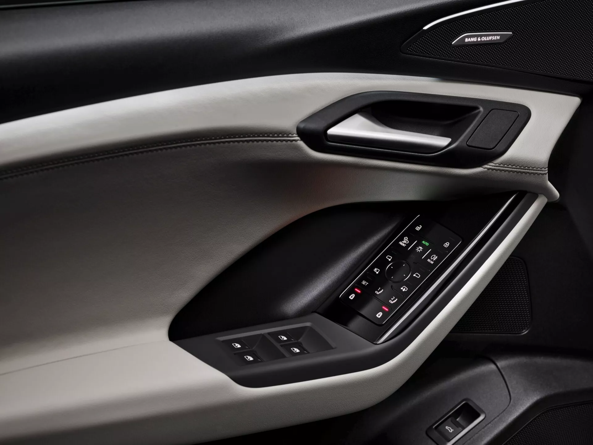 Vue rapprochée du panneau de porte intérieur de l'Audi Q6 e-tron 2024, mettant en avant les éléments de conception et les fonctionnalités. Le panneau de porte, capturé sous un angle diagonal, révèle différents matériaux et textures, comprenant une section supérieure douce au toucher avec des coutures apparentes, une garniture rigide abritant une poignée de porte ergonomique et un accoudoir rembourré avec un panneau de commande rétroéclairé pour les vitres et les réglages des rétroviseurs latéraux. Sous l'accoudoir, un système de haut-parleurs de marque indique un système audio premium. Le schéma de couleurs inclut un design bicolore, améliorant les qualités esthétiques et fonctionnelles.