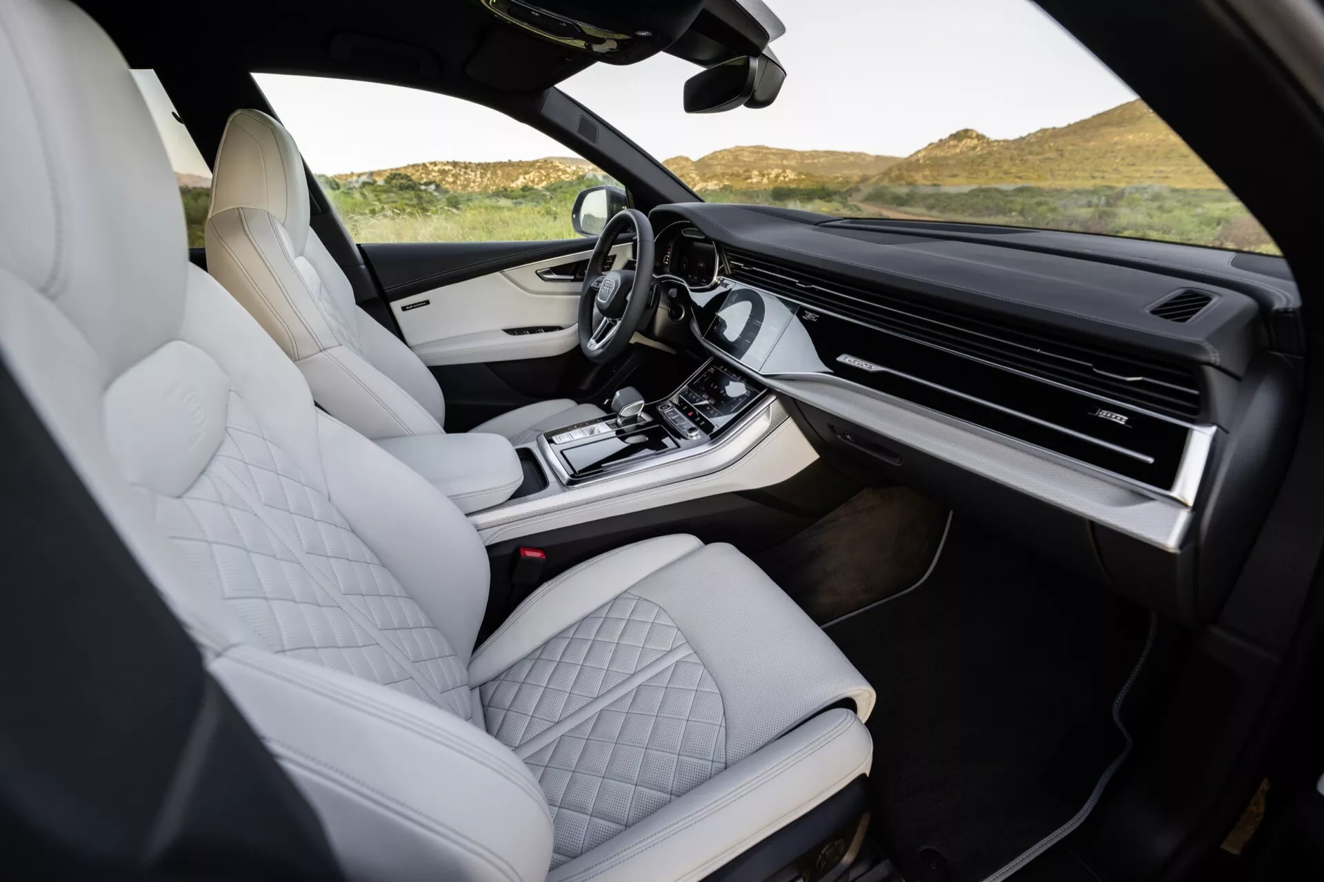 Intérieur de l'Audi Q8 2023 (4M-Facelift) présentant des sièges en cuir matelassé blanc, un design de console centrale haut de gamme, un système d'infodivertissement à écran tactile expansif, et des fonctionnalités modernes et ergonomiques, pris depuis le côté passager