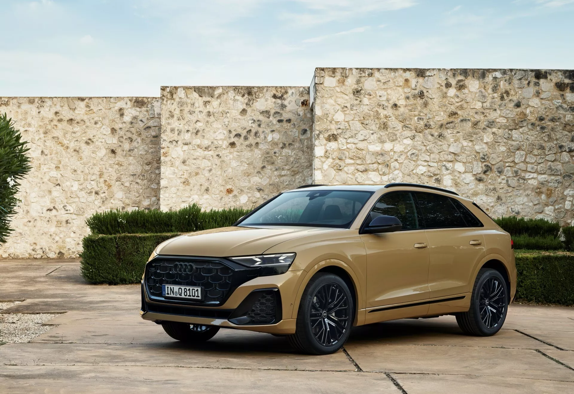 SUV moderne Audi Q8 2023 (4M-Facelift) en or tamisé, garé dans une cour historique montrant calandre avant, phares élégants et profil latéral sportif avec caractéristiques technologiques et éléments de design de luxe sous lumière naturelle