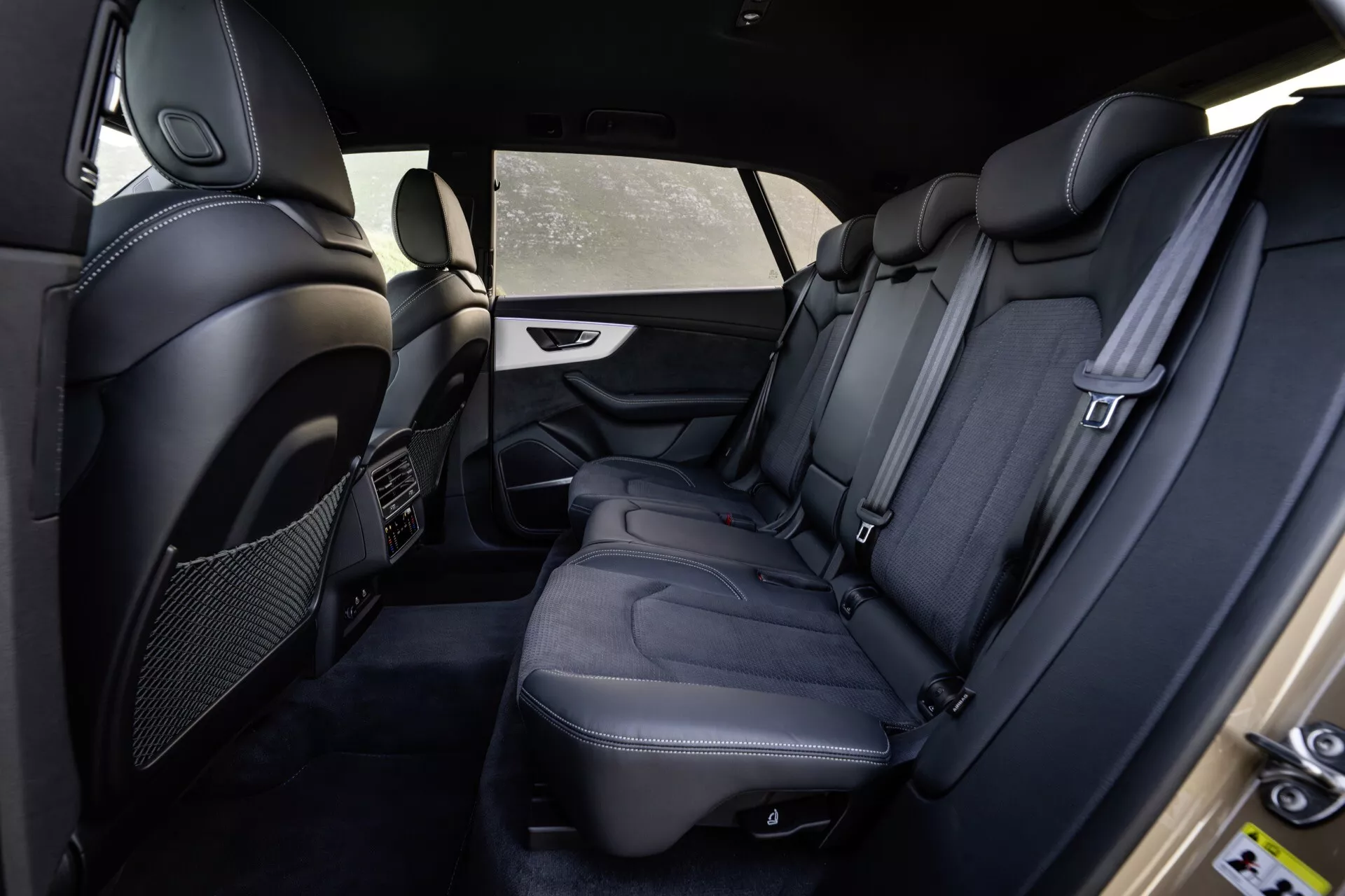 Intérieur de l'Audi Q8 4M-Facelift 2023 montrant le compartiment passagers arrière depuis le côté du conducteur avec des sièges en cuir noir haut de gamme, coutures détaillées, commodités de luxe et fonctionnalités de sécurité