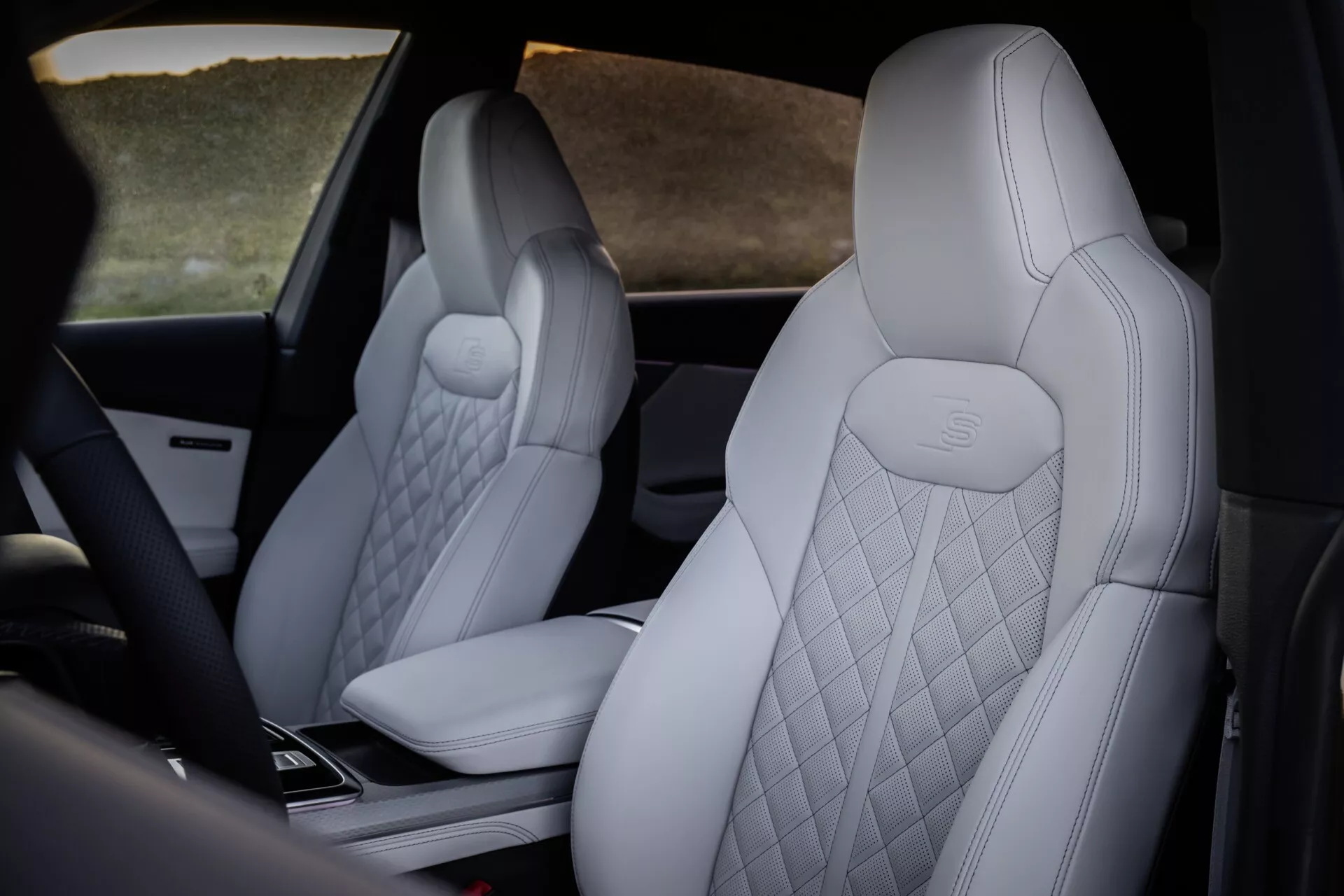 Vue intérieure de l'Audi Q8 2023 (4M-Facelift) mettant en avant les sièges avant luxueux avec une garniture diamantée de couleur claire et le logo Mercedes-Benz en relief, aperçu de la console centrale high-tech depuis une perspective arrière décentrée.
