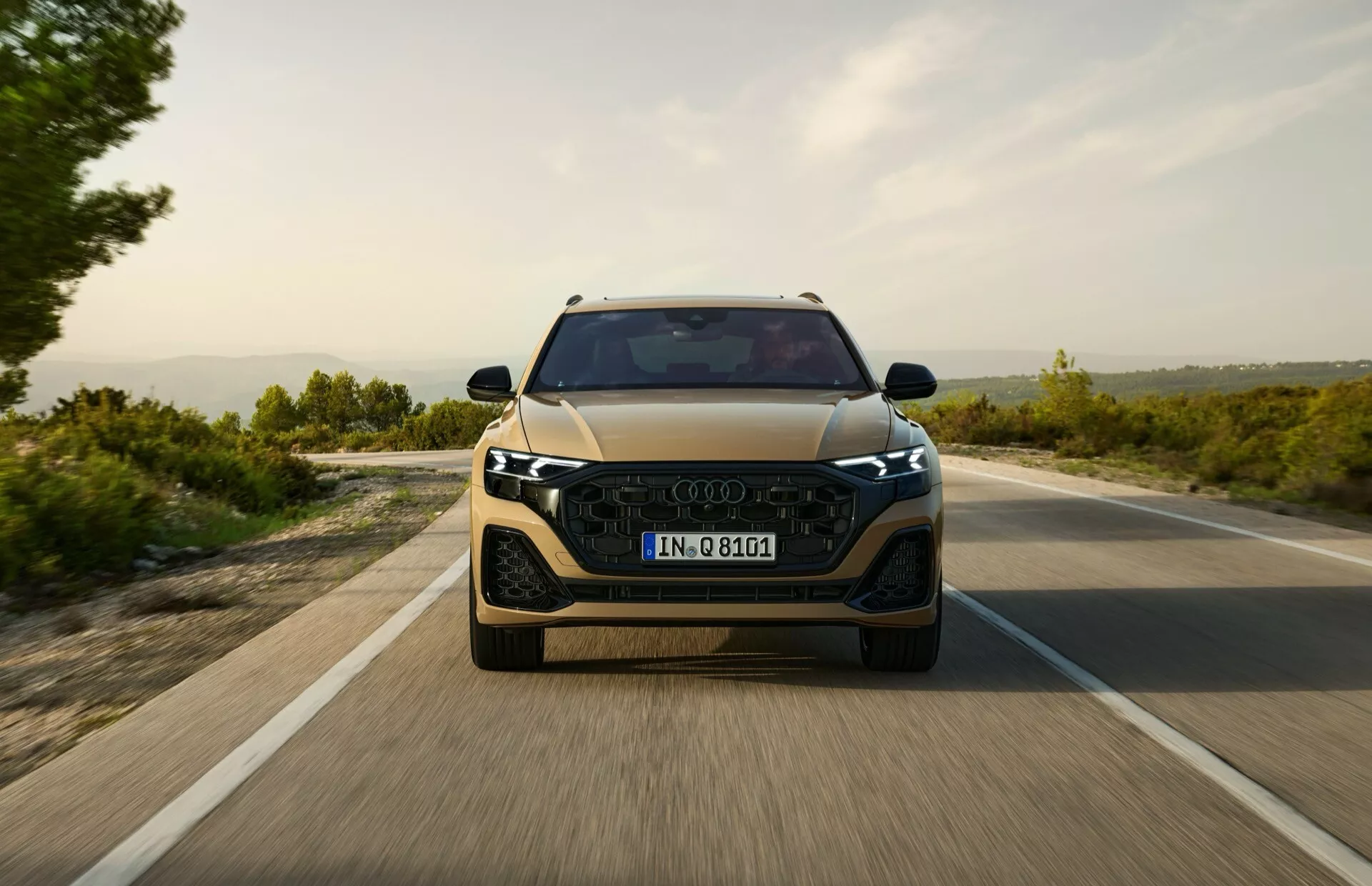 Vue frontale d'une voiture moderne roulant sur une route ouverte tôt le matin ou en fin d'après-midi, exhibant des phares avant élégants à LED, une grille saillante et des indices de systèmes d'assistance au conducteur avancés