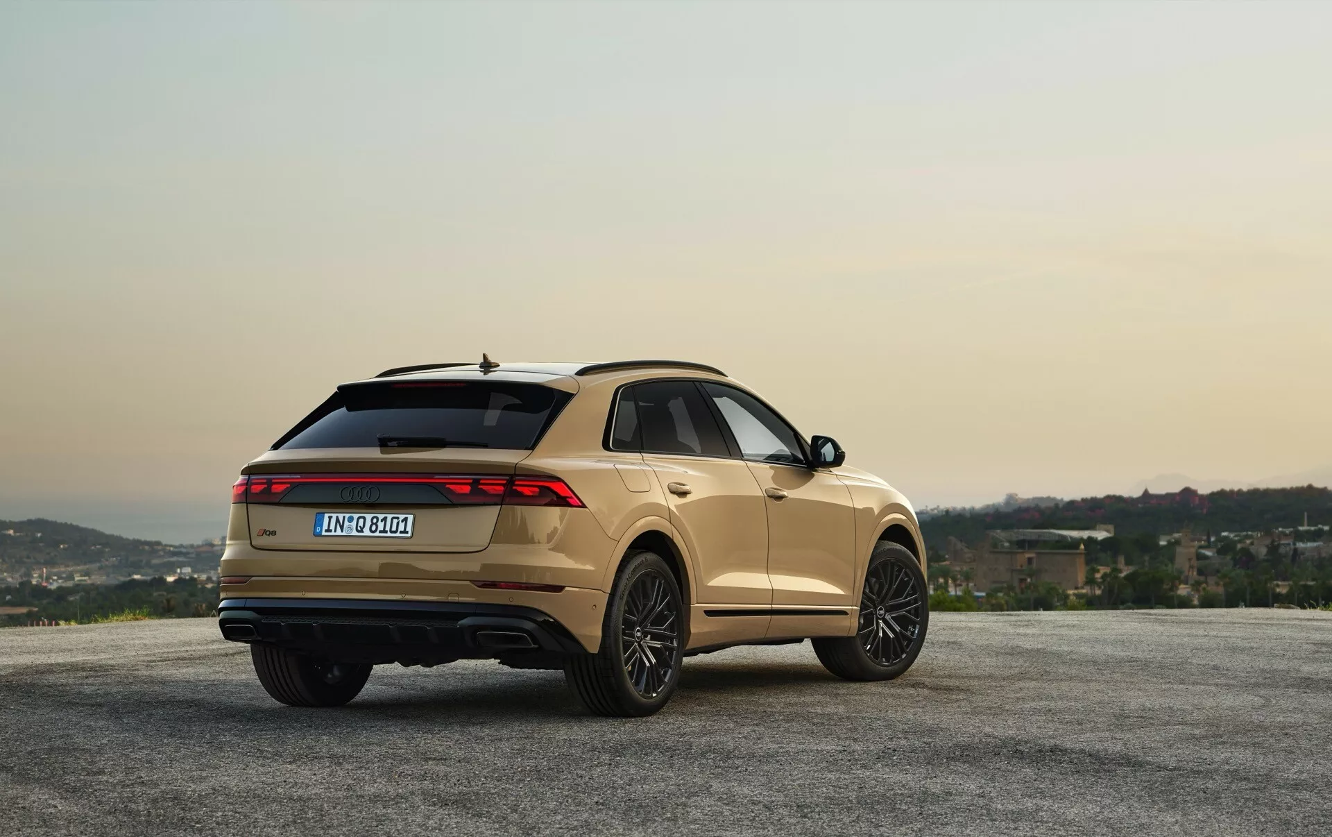 Audi Q8 2023 (4M-Facelift) finition métallique stationnée sur point de vue panoramique avec collines et ciel à l'aube/crépuscule, montrant angle arrière trois quarts pour vue de design et fonctionnalités