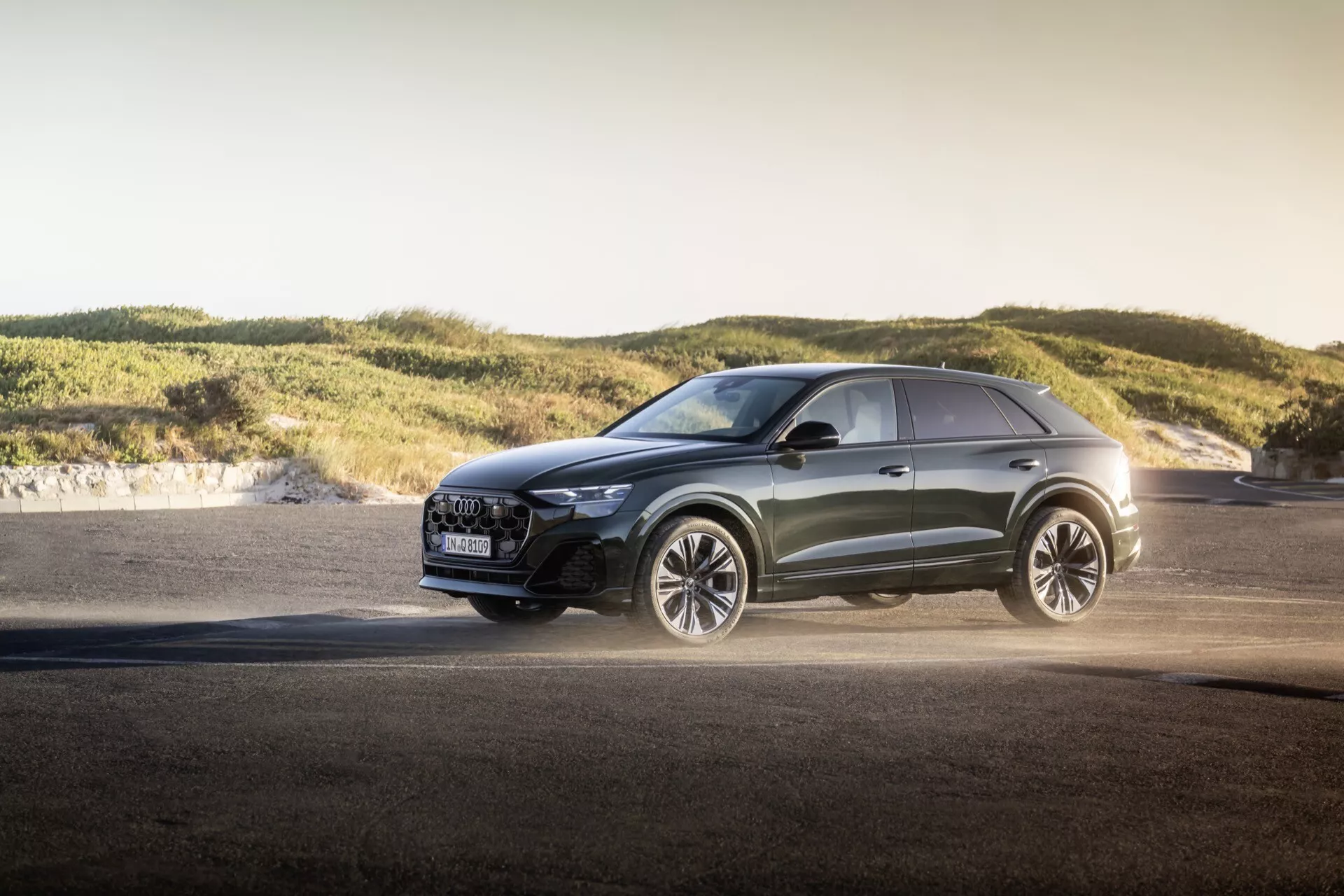 Crossover moderne Audi Q8 2023 (4M-Facelift) en extérieur pendant l'heure dorée, présentant des phares LED avancés, une grille de luxe avec fonctionnalités de sécurité, de grandes roues en alliage axées sur la performance, une peinture métallique et des lignes de design sportives sur fond d'asphalte et de douces collines, soulignant des capacités polyvalentes et un design