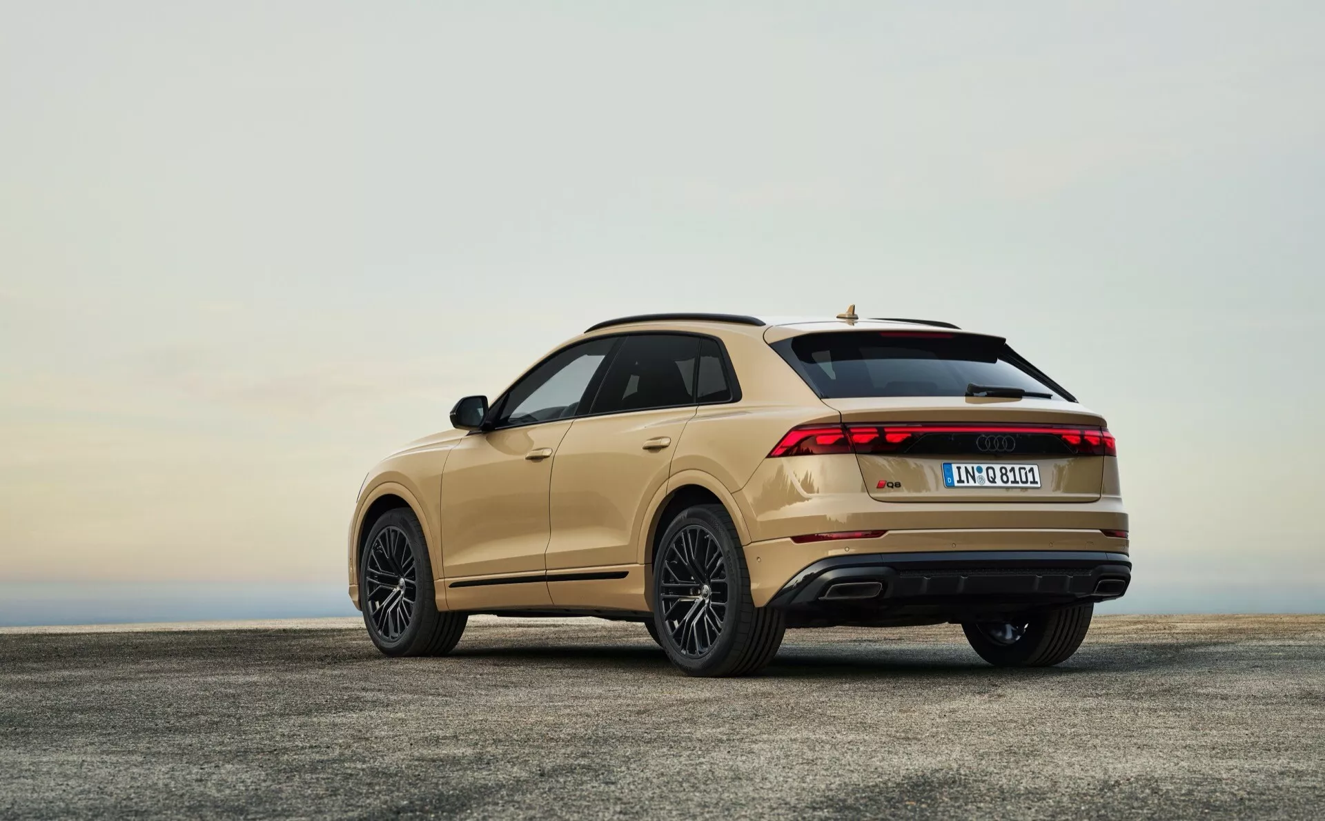 Vue arrière trois quarts du Audi Q8 4M facelift 2023 sur surface en béton sous ciel d'aube ou crépuscule mettant en évidence feux arrière LED, jantes en alliage, becquet de toit, toit ouvrant panoramique et sorties d'échappement doubles