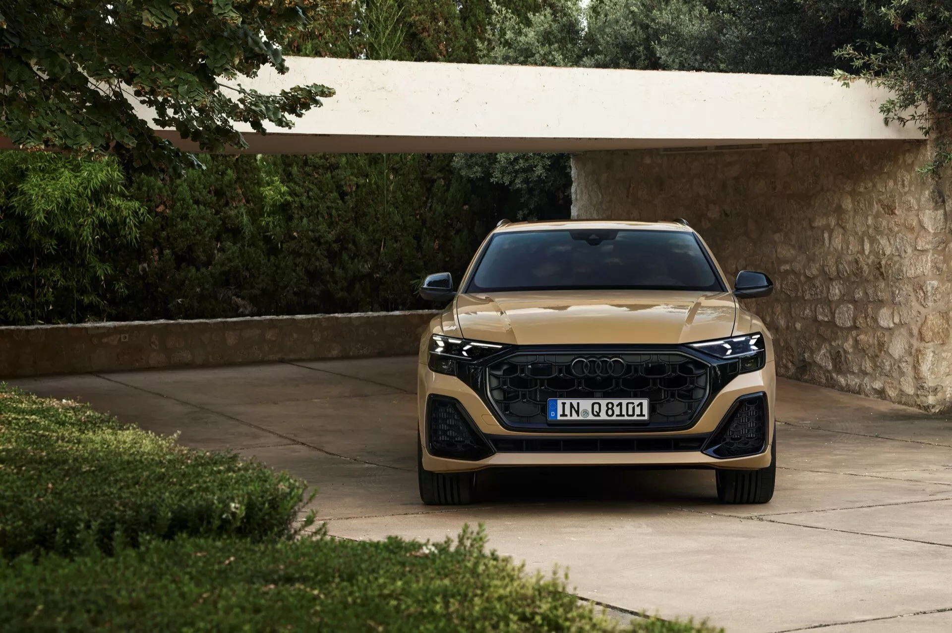 Audi Q8 2023 (4M-facelift) présentée depuis un angle frontal, mettant en valeur sa large grille, ses phares LED élégants et sa finition métallique, mise en scène dans une allée entourée de verdure luxuriante
