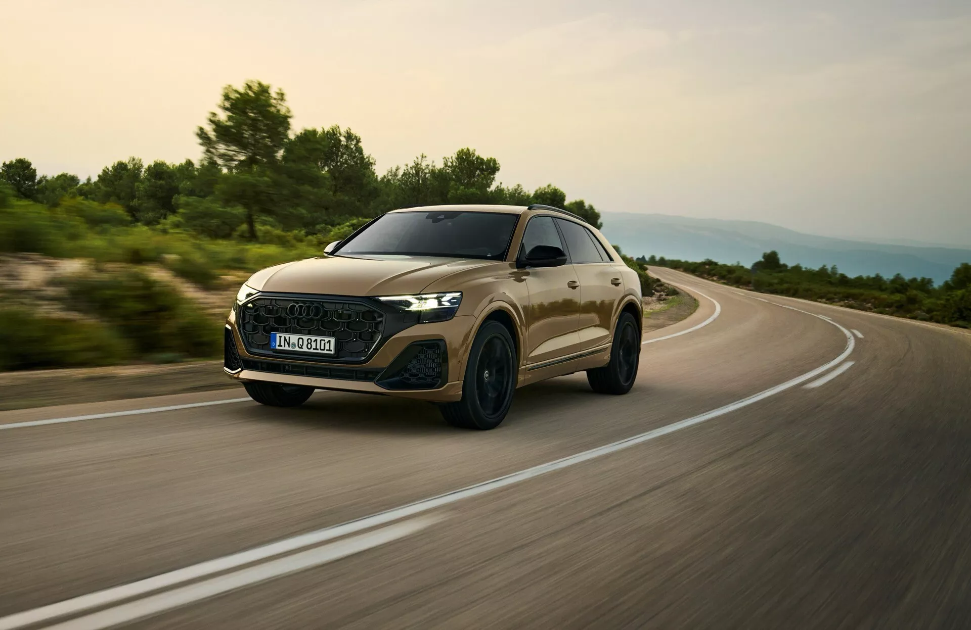 Audi Q8 2023 (modèle 4M facelift) capturée dans une scène de conduite dynamique, mettant en avant sa grille avant aérodynamique, phares LED, et profil élégant depuis un angle bas avant trois quarts suggérant vitesse et caractéristiques premium