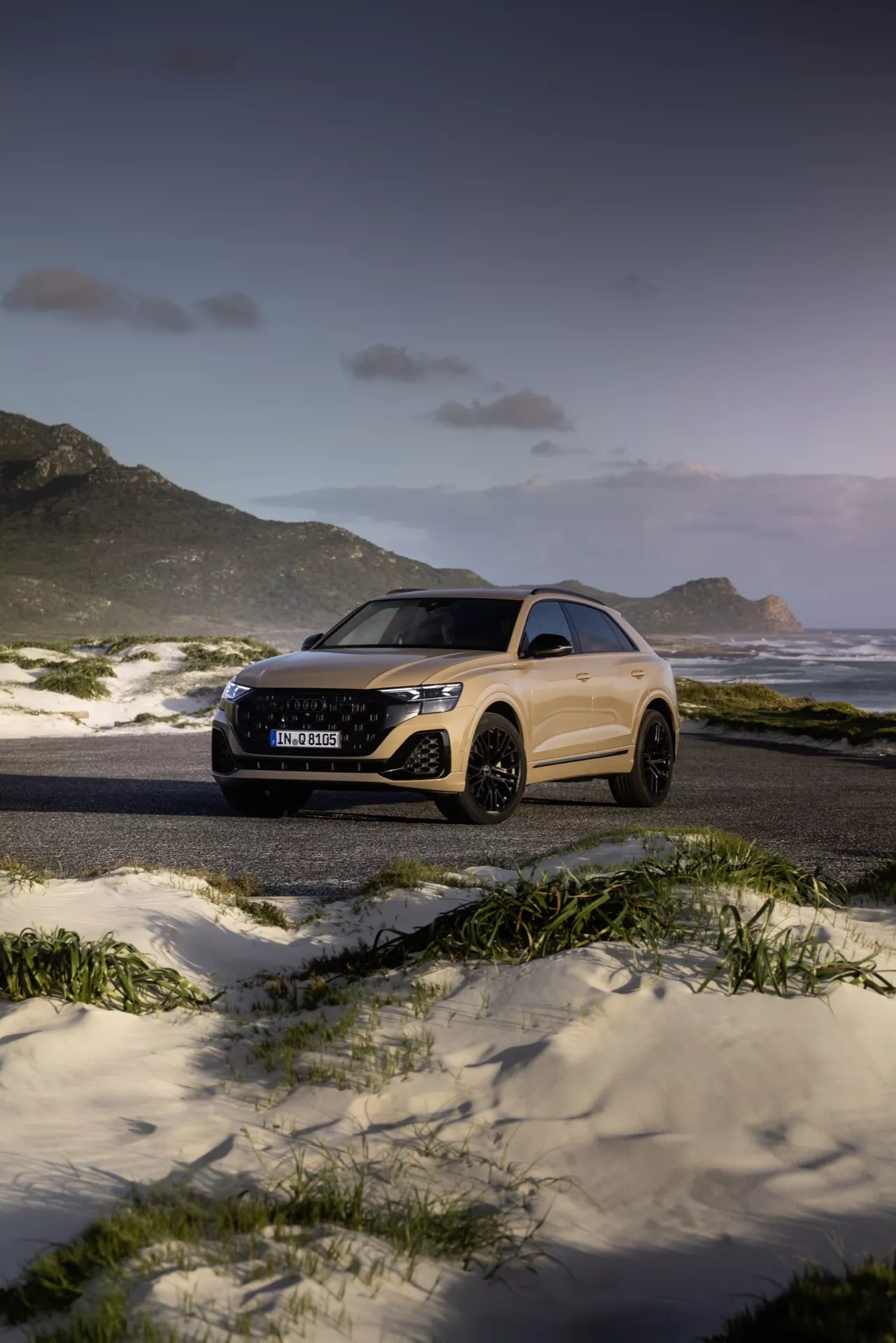 Audi Q8 2023 (4M-Facelift) dans un paysage majestueux de plage et de montagne au crépuscule, présentant son design élégant et ses caractéristiques avancées telles que les phares LED et les grandes roues en alliage, sous un angle de trois quarts avant et latéral
