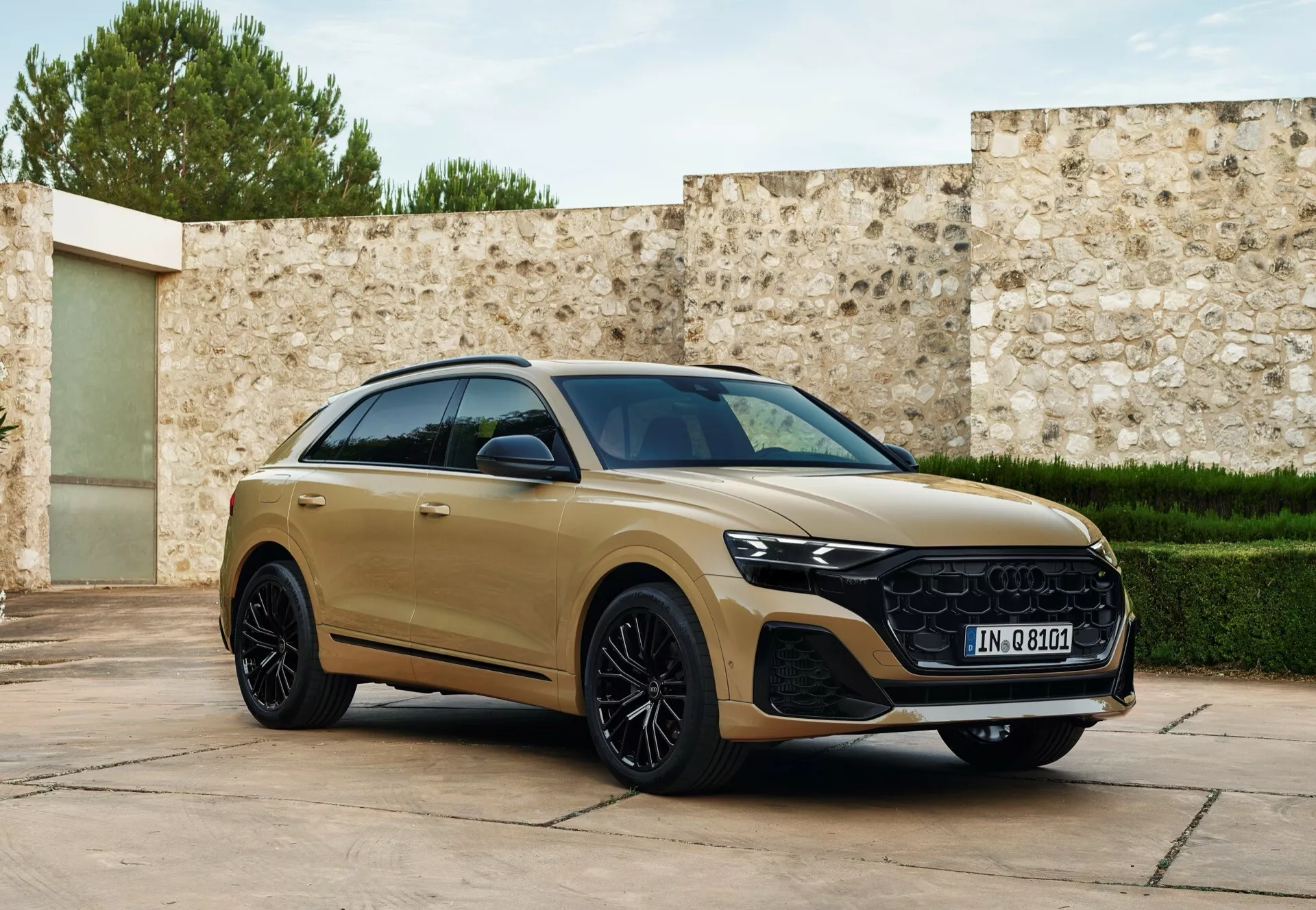 Vue avant trois quarts de l'Audi Q8 2023 (4M-facelift) en teinte dorée, montrant son profil latéral aérodynamique, sa grille distinctive, ses phares LED et ses roues en alliage de luxe, garée avec une légère orientation vers l'appareil photo sur un arrière-plan raffiné