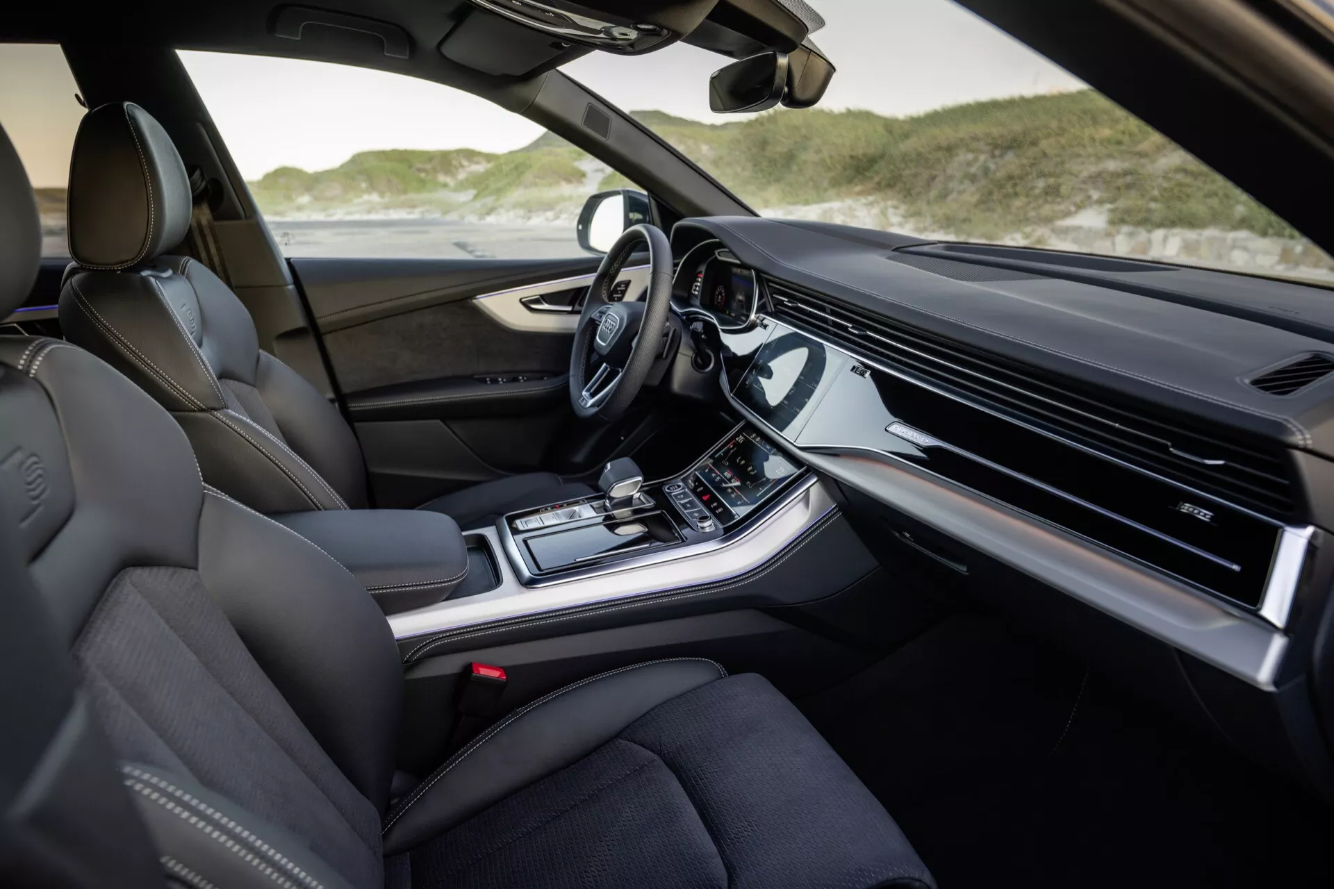 Vue intérieure de l'Audi Q8 2023 (4M-Facelift) côté passager avec sièges en cuir de luxe, tableau de bord avancé avec écran d'infotainment intégré, console centrale avec commandes climatiques et de mode de conduite, levier de vitesse automatique moderne et volant équipé de technologies