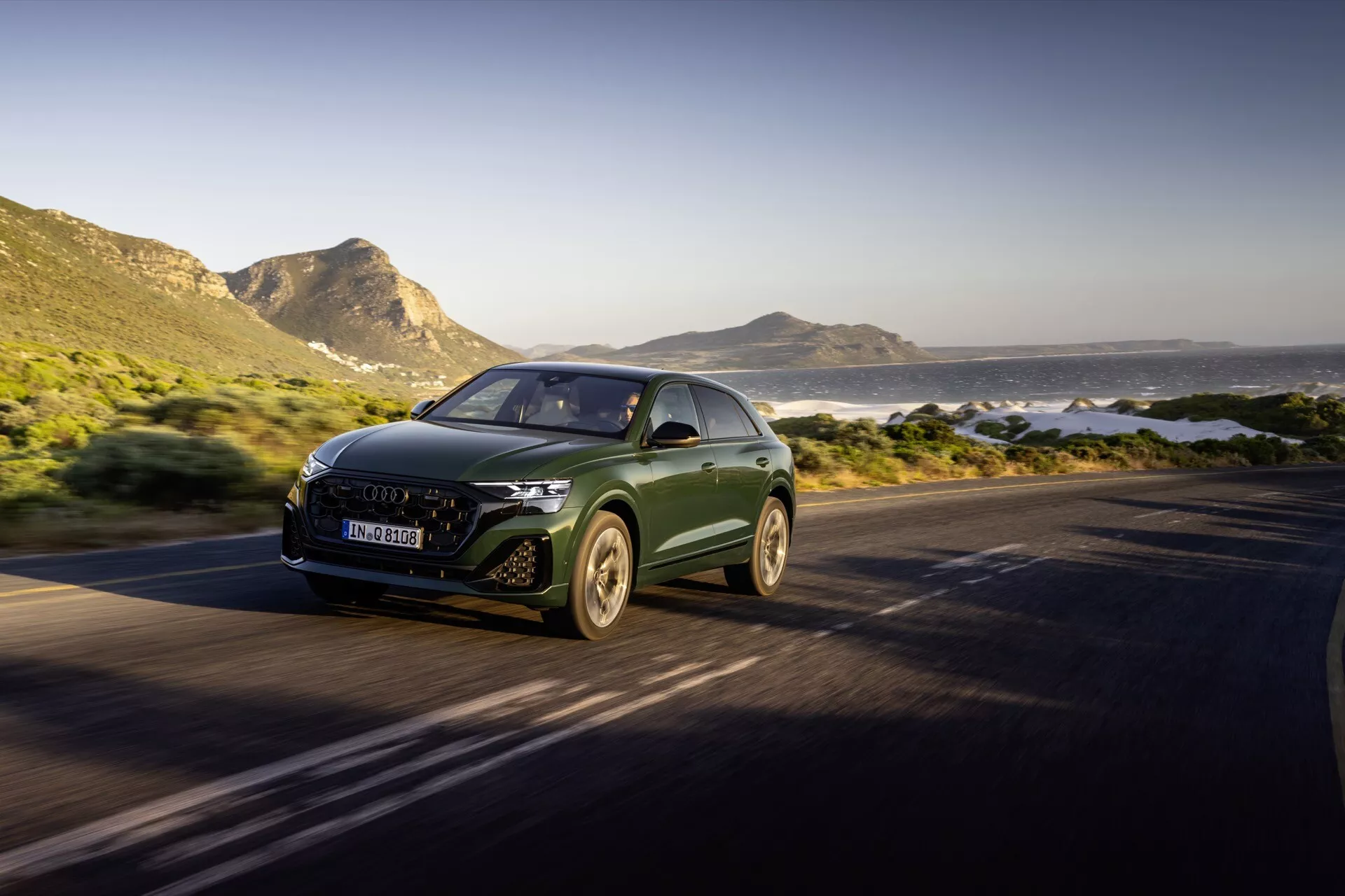 Audi Q8 4M-Facelift 2023 roulant sur une route côtière, mise en évidence par son design aérodynamique, ses phares LED et l’emblème du fabricant sur la grille, capturée depuis un angle avant de trois quarts montrant le SUV de luxe en mouvement contre un arrière-plan pittoresque