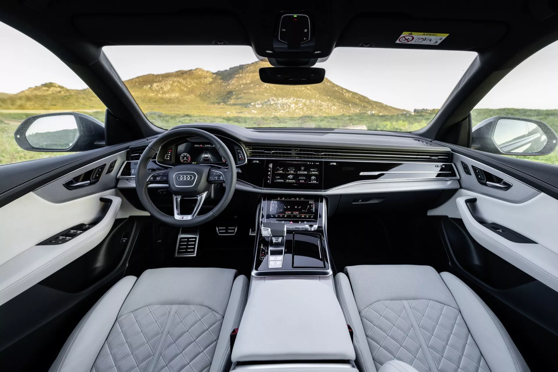 Vue intérieure de l'Audi Q8 2023 (4M-Facelift), présentant la cabine avant depuis une perspective à la première personne, mettant en évidence le volant sportif multifonction, le cluster d'instruments numériques, l'écran tactile d'infodivertissement étendu, les sièges en cuir de couleur claire avec couture en forme de diamant et les détails de finition haut de gamme.
