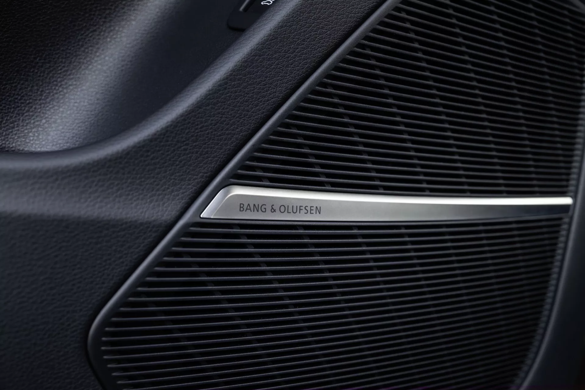 Gros plan sur la grille du haut-parleur Bang & Olufsen à l'intérieur de l'Audi Q8 2023 (4M-Facelift), montrant le motif fin en maille du système audio premium et le logo métallique poli sur fond noir.