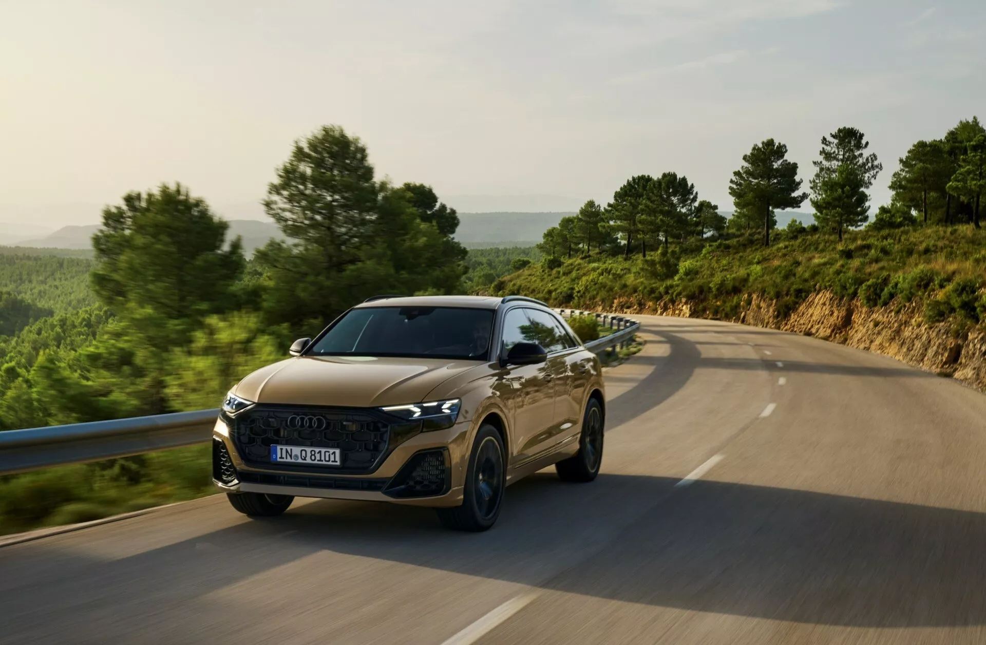 Audi Q8 4M Facelift 2023 circulant sur une route de campagne, présentant des phares LED, une grille hexagonale, des contours de capot sportifs et une technologie avancée d'assistance au conducteur