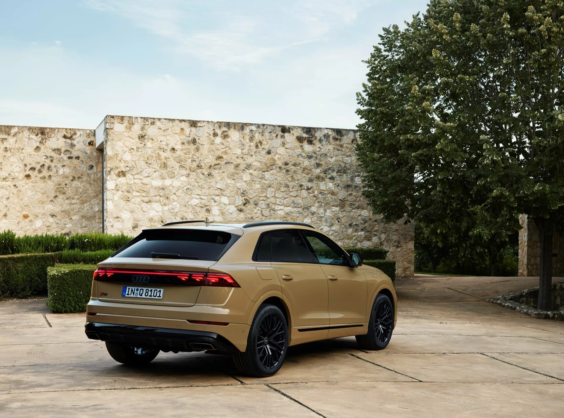 Modèle Audi Q8 4M facelift 2023 garé à l'extérieur, capturé sous un angle arrière de trois quarts mettant en lumière ses feux arrière à LED, ses jantes en alliage sombre à multiples branches, sa ligne de toit inclinée et ses doubles tuyaux d'échappement contre un fond de cour en pierre