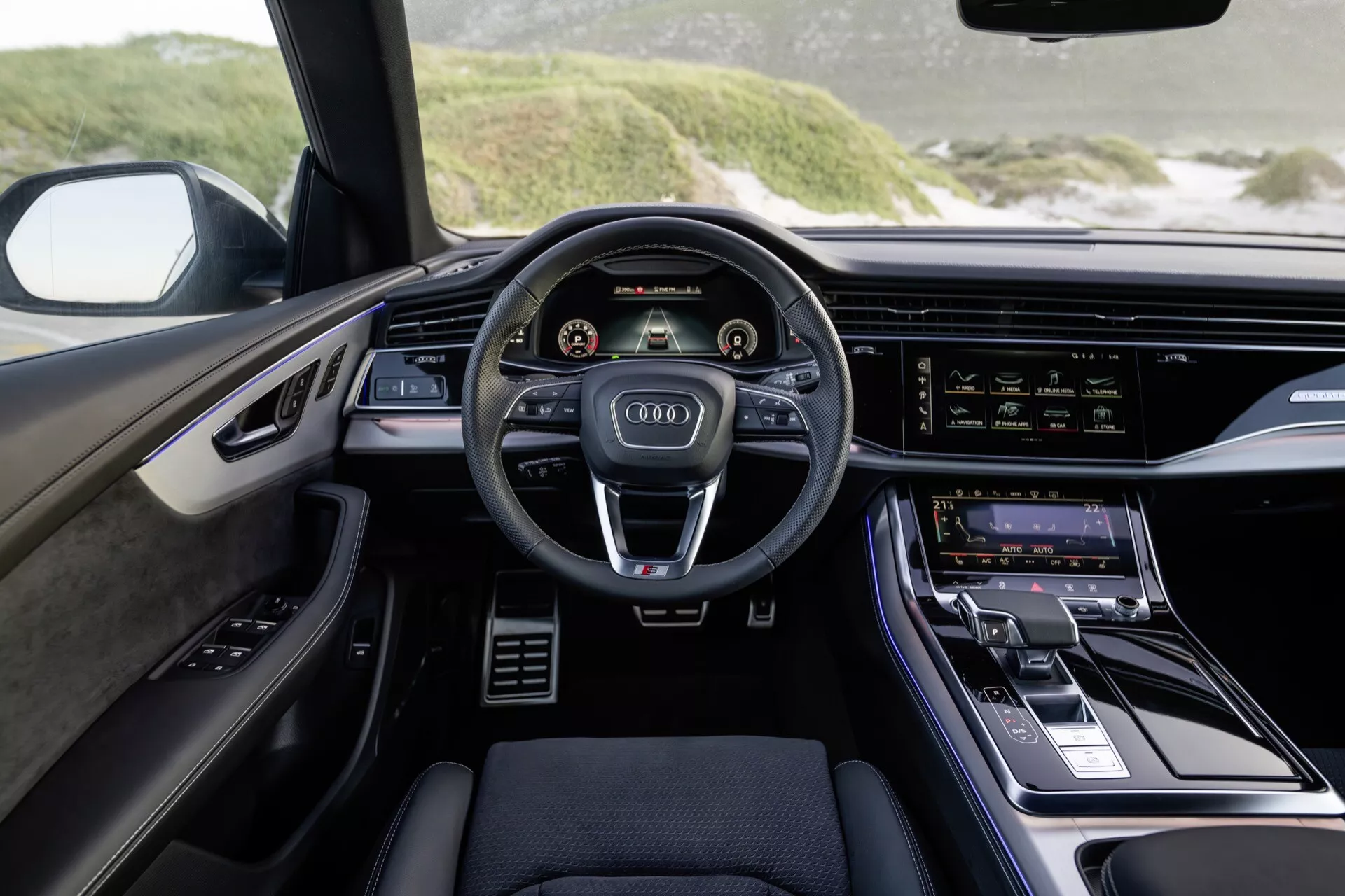 Vue intérieure de l'Audi Q8 2023 (4M-Facelift) du point de vue du conducteur, mettant en évidence le tableau de bord moderne, le volant à trois branches avec boutons de commande, les doubles affichages numériques pour le cluster d'instruments et le système d'infodivertissement, et les accents de design luxueux.
