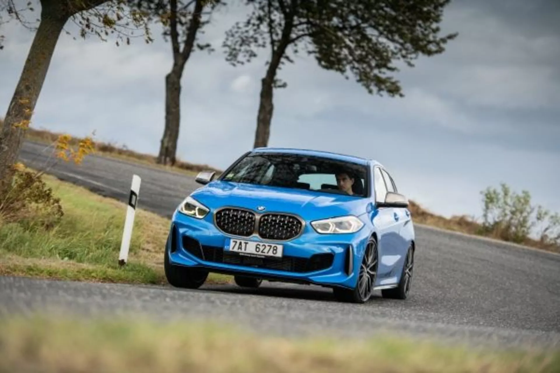 Berline sportive bleue BMW Série 1 M Performance 2019 capturée sous un angle latéral avant bas et incliné soulignant sa façade avant agressive avec des grilles rénales emblématiques, des phares LED élégants, de grandes entrées d'air pour le refroidissement des performances, une suspension sportive basse, en mouvement autour d'un virage démontrant une maniabilité dynamique, avec des rétroviseurs latéraux aérodynamiques, de grandes roues alliage et des pneus à profil bas mettant en évidence le statut sportif et les capacités d'adhérence.