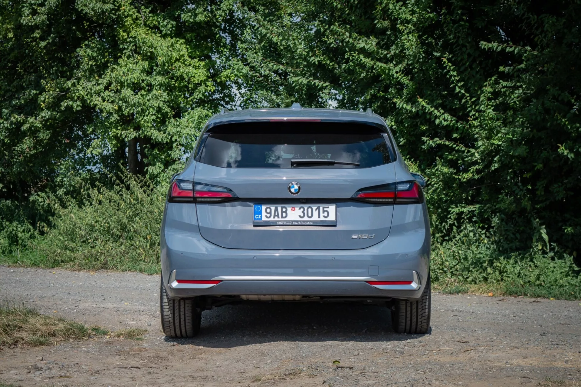 Vue arrière de la BMW Série 2 Active Tourer 2022, mettant en avant les embouts d'échappement jumeaux, les capteurs de stationnement arrière, et les feux arrière LED sous un éclairage naturel avec un arrière-plan de verdure suburbaine.