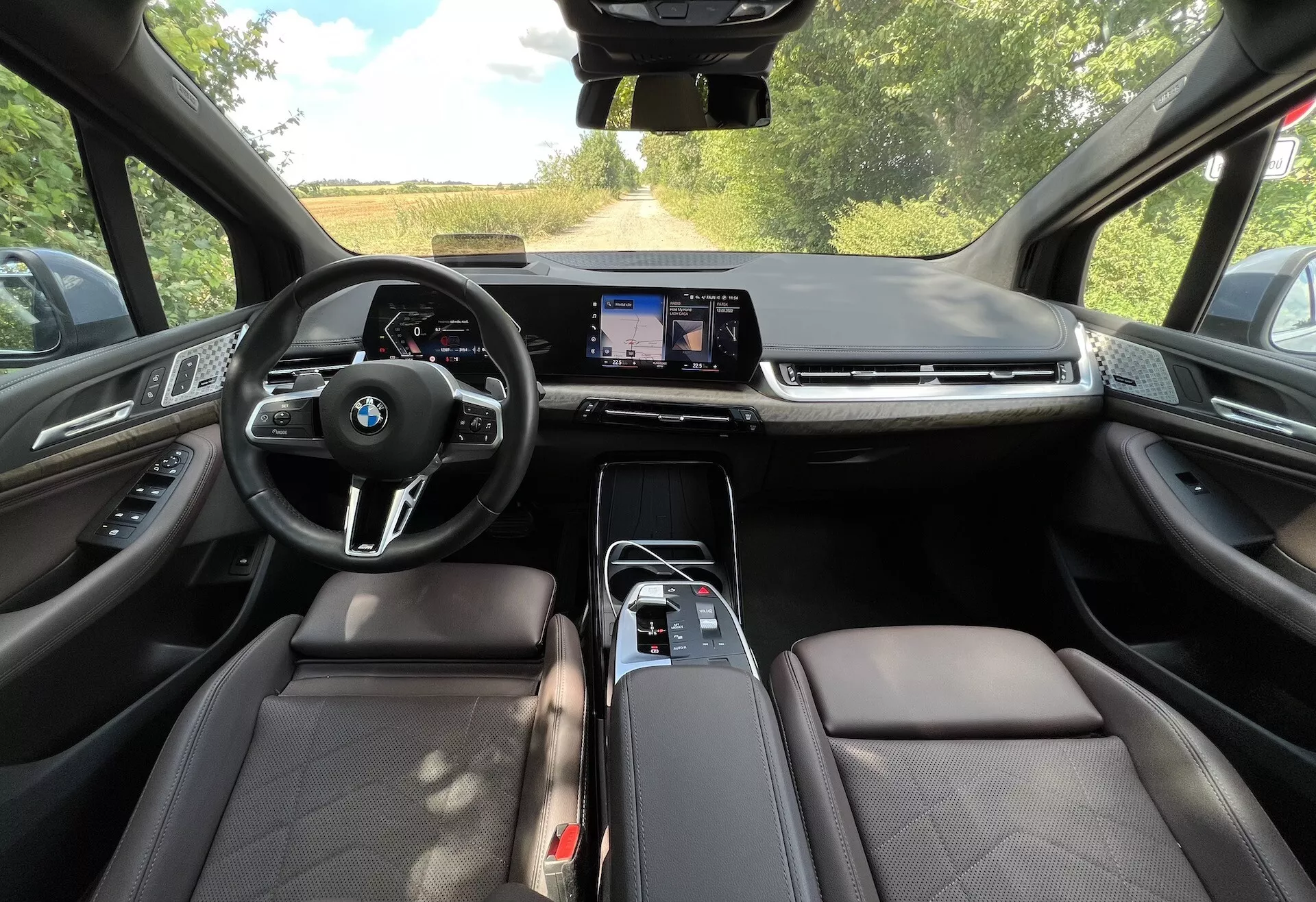 Vue intérieure d'une BMW Série 2 Active Gran Tourer 2022 montrant le volant multifonction avec logo BMW, grand écran tactile d'infodivertissement, sièges en cuir et fonctionnalités technologiques avancées du point de vue du siège conducteur.