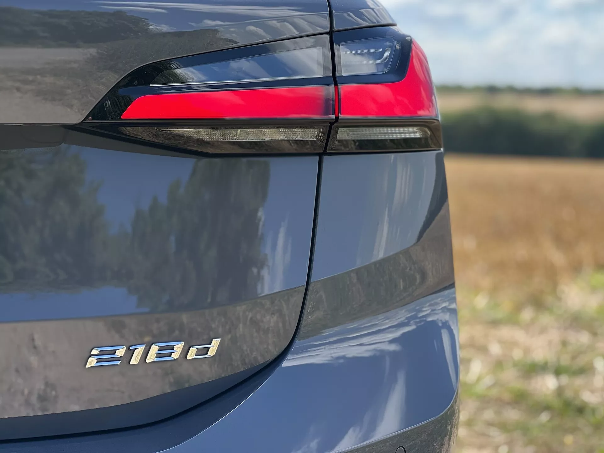 Vue rapprochée du côté arrière gauche du BMW Série 2 Active Tourer 218d mettant en lumière le bloc de feux arrière LED, le badge du modèle et la finition peinture métallique en lumière du jour