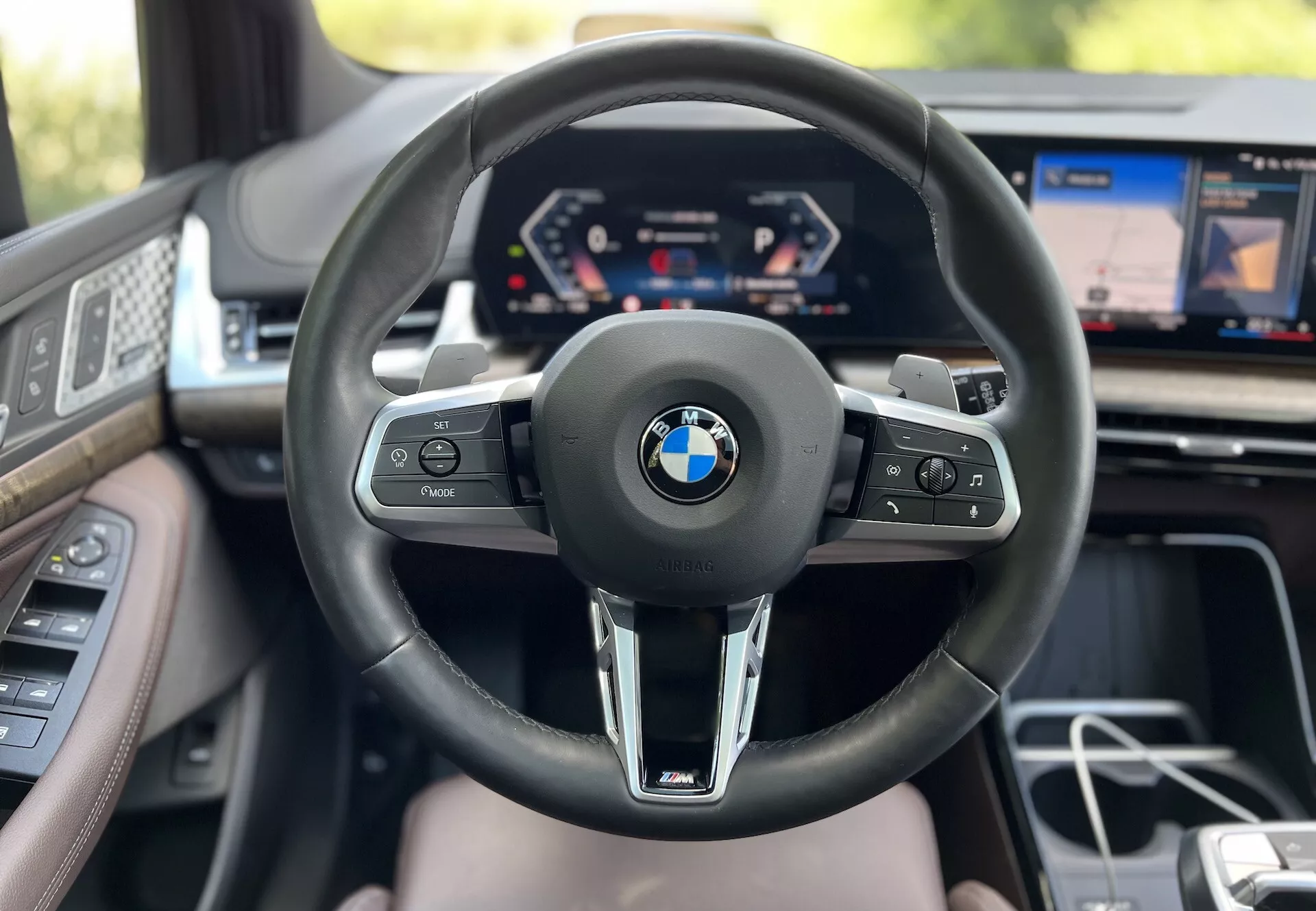 Vue intérieure de la BMW 2 Series Active Tourer 2022 du point de vue du conducteur avec volant visible arborant le logo BMW et le branding M, cluster d'instruments numérique, et affichage partiel de l'infodivertissement mettant en évidence la technologie avancée du véhicule et les caractéristiques de luxe