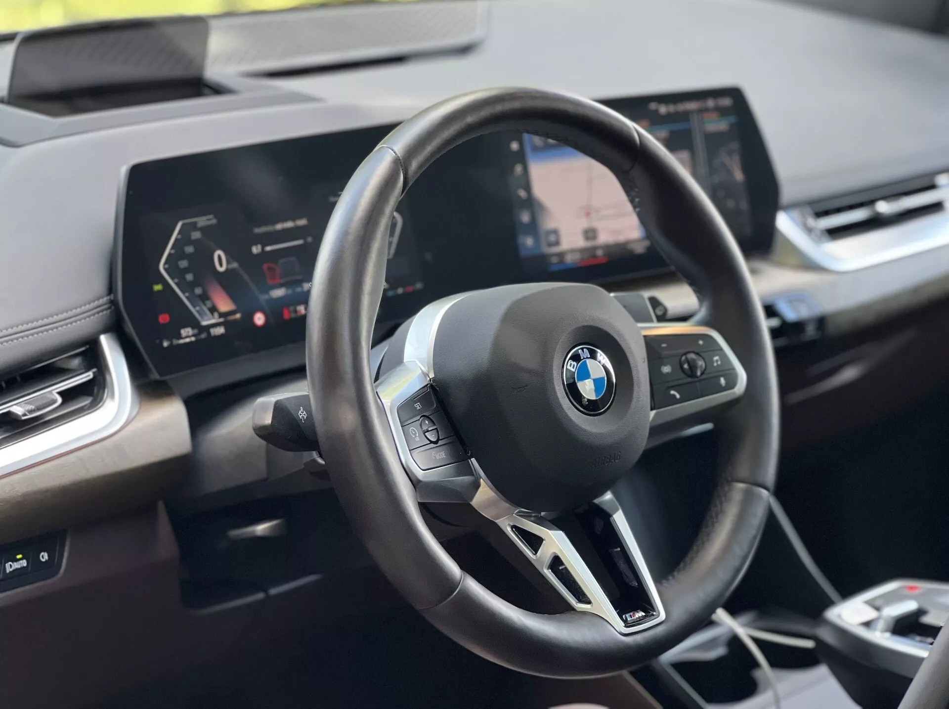 Photo intérieure de la BMW Série 2 Active Tourer 2022 : volant avec emblème BMW et commandes multifonctions, tableau de bord numérique, et écran central d'infodivertissement avec système de navigation, du point de vue du conducteur
