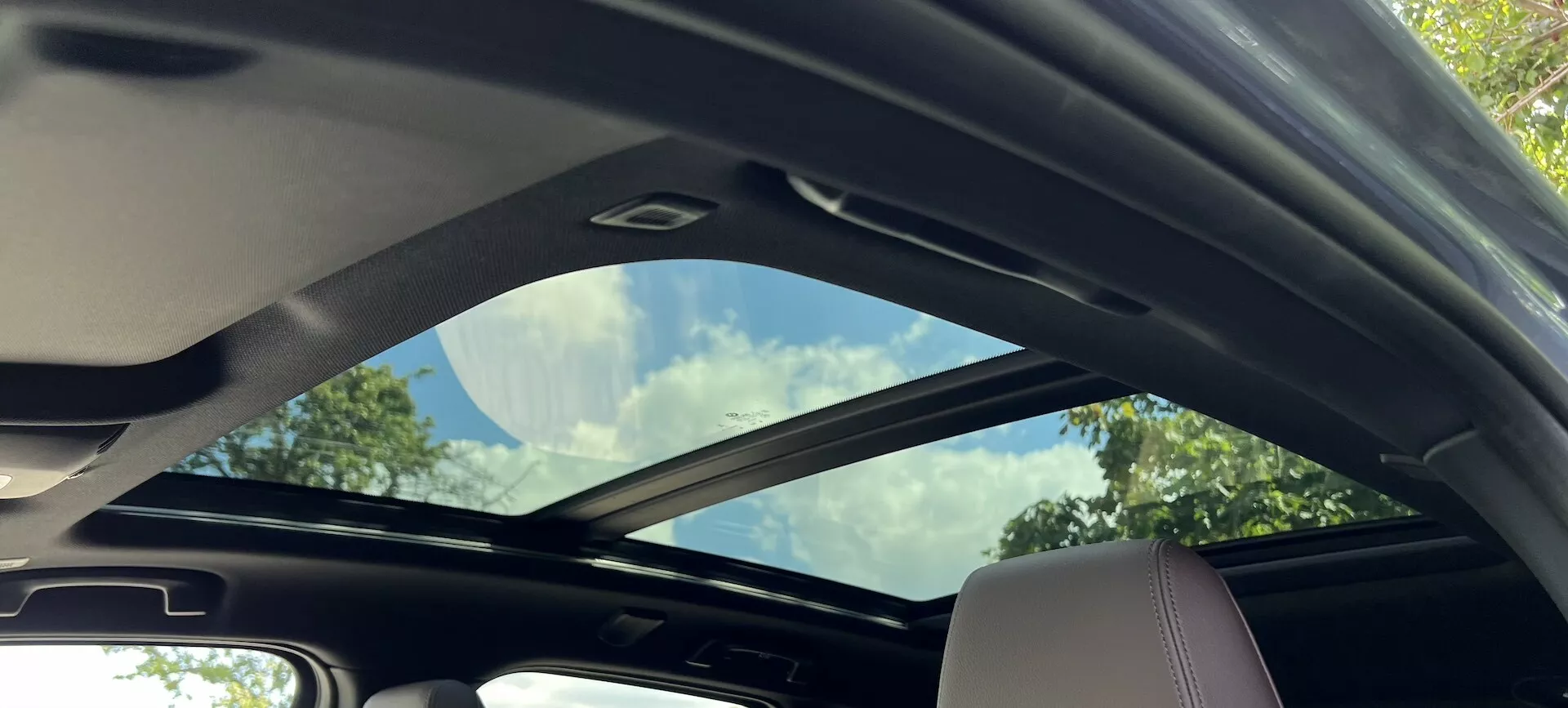 Vue intérieure du BMW Série 2 Active Tourer 2022 montrant le toit ouvrant panoramique partiellement ouvert et les détails intérieurs de couleur claire, soulignant l'espace et les équipements de luxe.