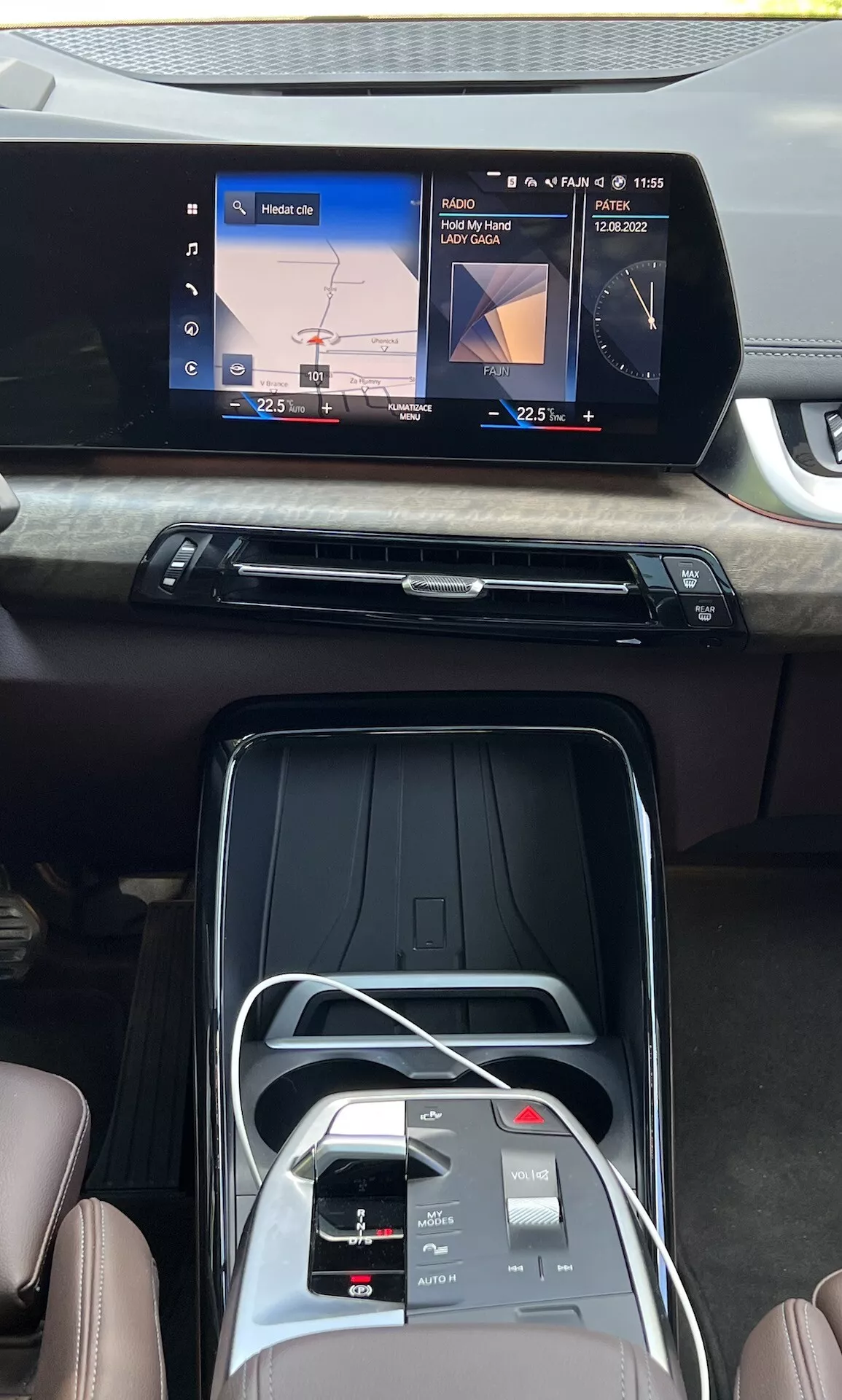 Vue intérieure de la BMW Série 2 Active Gran Tourer 2022 montrant la console centrale, l'écran tactile d'infodivertissement grand écran avec navigation et lecture de médias, aération élégante avec finition en bois, boutons de contrôle du climat, interface tactile, sélecteur de vitesse électronique et sièges en similicuir haut de gamme