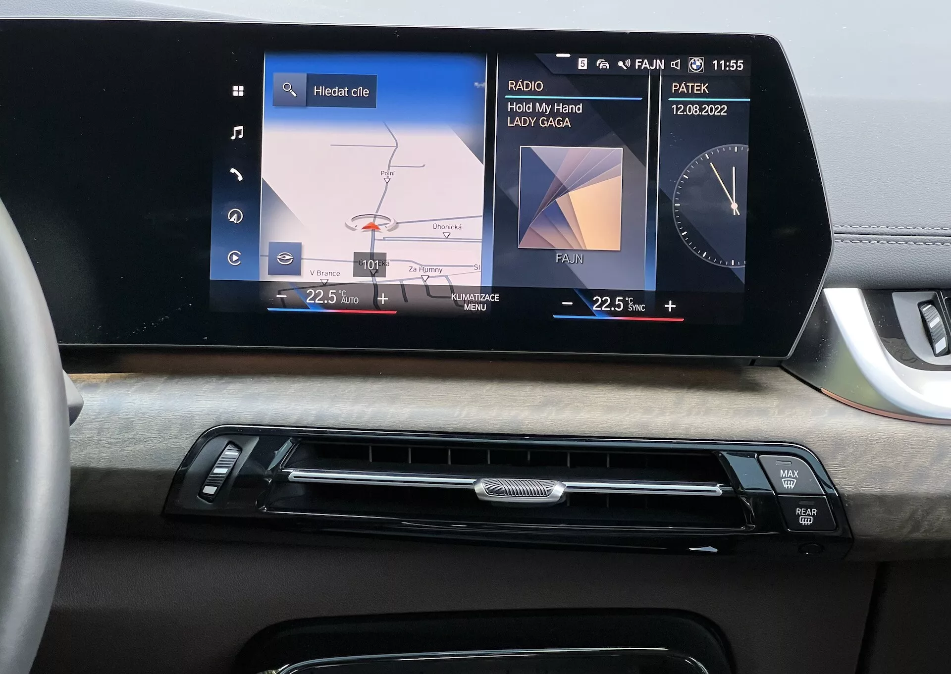Intérieur de la BMW Série 2 Active Tourer 2022 concentré sur le tableau de bord avec un système d'infodivertissement central affichant un menu graphique de la voiture pour les réglages des phares et l'affichage des médias ‘Hold My Hand’ de Lady Gaga, visibilité de la date et de l'heure, complété par une finition en bois et des boutons de contrôle climatique