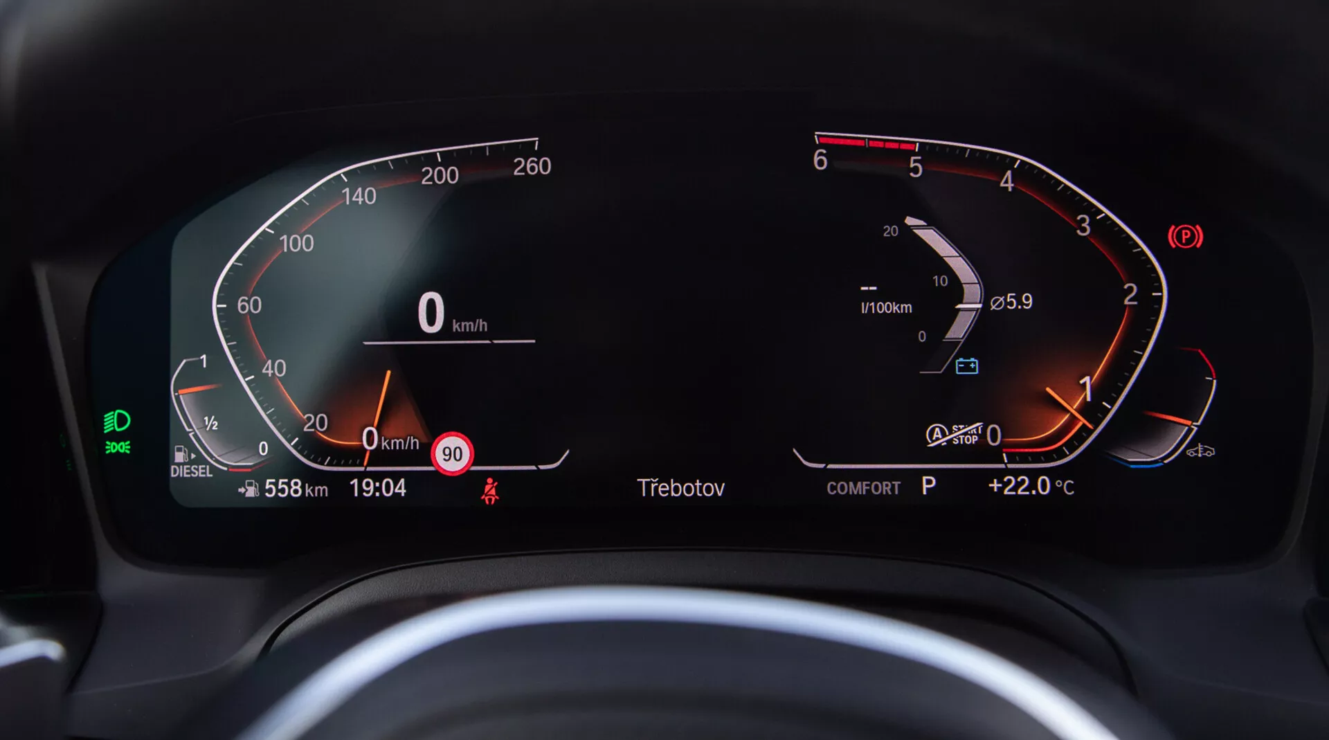 Vue rapprochée du tableau de bord numérique de la BMW 2 Series Coupe 2022, vue depuis le siège conducteur. Le compteur de vitesse numérique semi-circulaire à gauche va de 0 à 260 km/h, montrant que le véhicule est à l'arrêt. Le compte-tours à droite montre le moteur au ralenti juste au-dessus de 0 tr/min. Intégré dans le compte-tours se trouvent une jauge de carburant numérique presque pleine et une jauge de température du moteur indiquant une plage normale. L'affichage numérique central montre le compteur de kilométrage total à 558 km, vitesse à 0 km/h, avertissement de vitesse à 90 km/h, heure actuelle 19:04, indicateur de vitesse 'P' pour Park, et température extérieure +22,0 °C. Une icône verte d'assistance au maintien dans la voie, l'affichage du mode 'COMFORT', l'indicateur de carburant diesel et le rappel de la ceinture de sécurité sont également visibles.