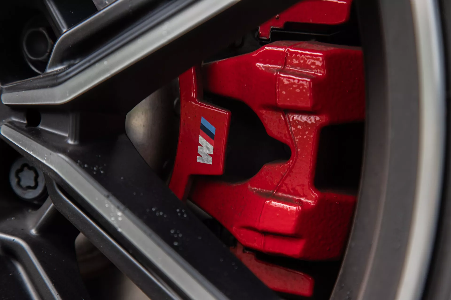 Vue rapprochée d'un étrier de frein rouge vif et d'un rotor sur la BMW Série 2 Coupé 2022, avec un design multipiston, un logo 'M', une jante en alliage léger sombre à plusieurs rayons et un pneu haute performance à profil bas. Le rotor ventilé améliore le refroidissement en conditions de freinage intense, capturé dans un style de photographie macro pour souligner les aspects de performance.