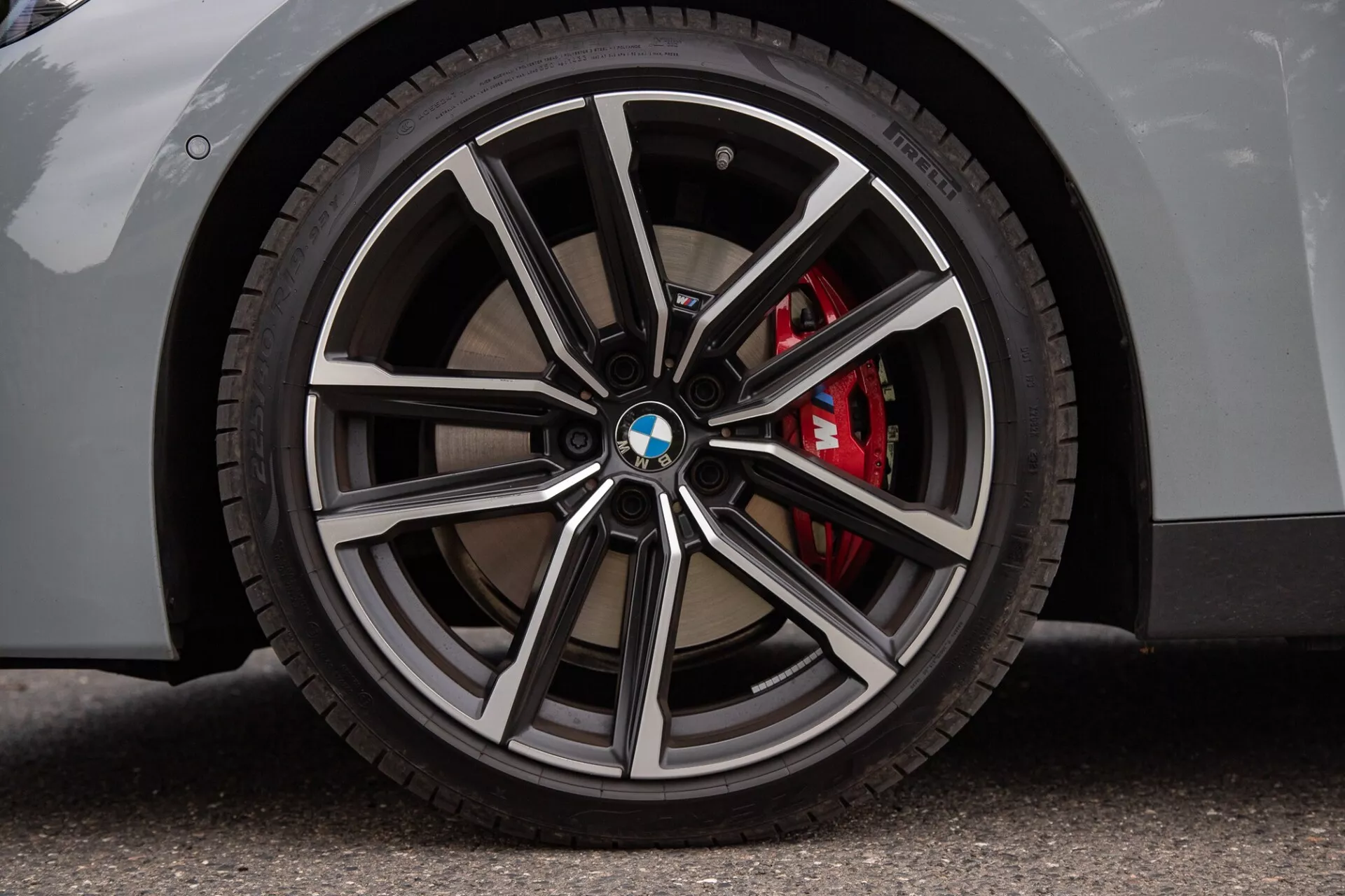 Gros plan sur une roue de BMW Série 2 Coupé avec une jante à rayons multiples aux finitions métalliques polies et sombres, un logo BMW sur l’enjoliveur, un pneu à profil bas et un étrier de frein rouge performant. La carrosserie claire sur une surface en asphalte met en évidence les aspects de luxe et de sportivité.