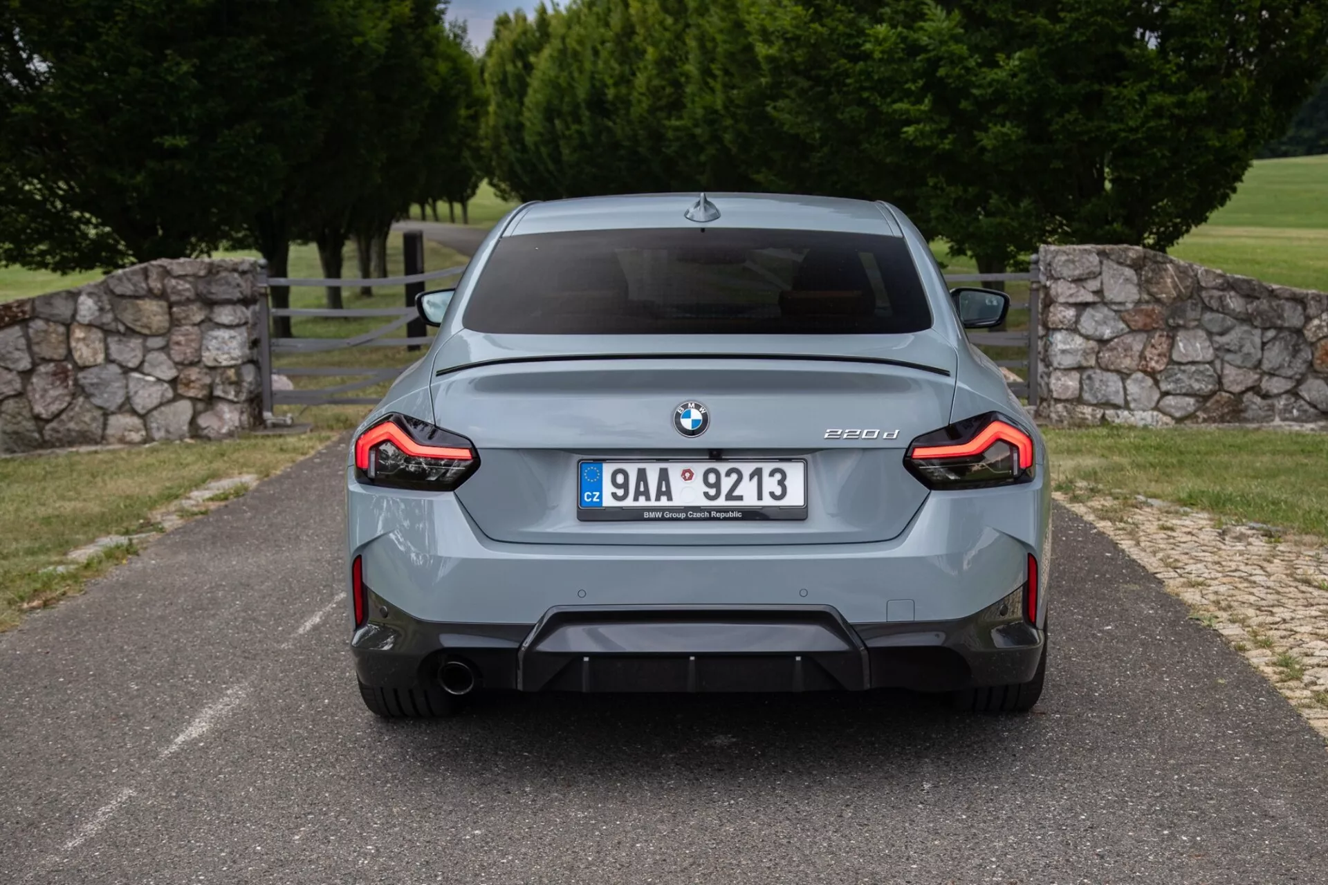 Vue arrière d'une berline BMW M3 grise (modèle G80) montrant l'emblème BMW, le badge M3 avec information sur le modèle G80, plaque d'immatriculation centrale, pare-chocs arrière sportif avec diffuseur intégré, embouts d'échappement doubles, feux arrière à LED en forme de L sur toute la largeur et élargisseurs d'ailes.