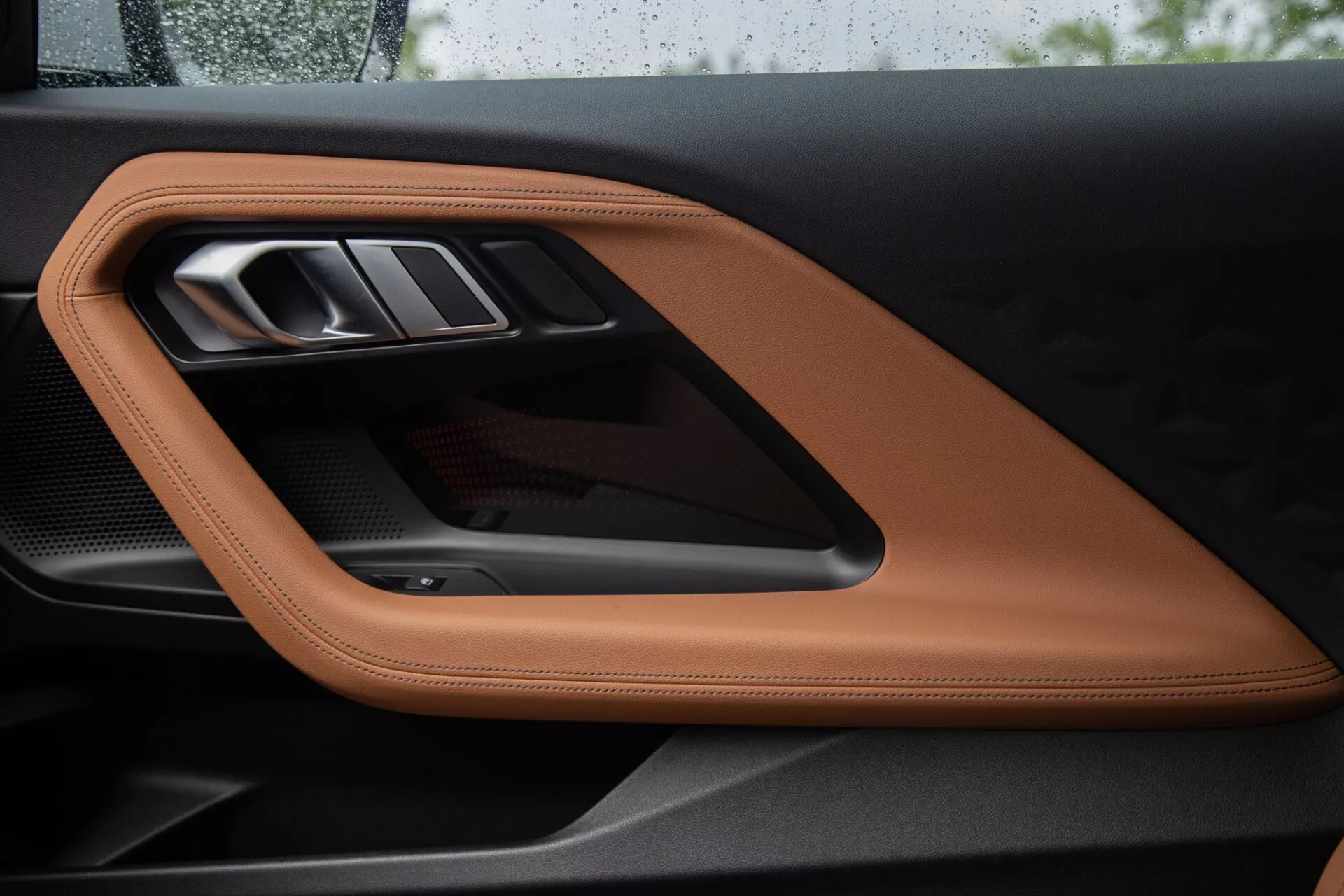 Gros plan sur le panneau de porte intérieur de la BMW Série 2 Coupé 2022, mettant en avant un cuir cousu de couleur tan ou cognac, une poignée de porte métallique élégante et une garniture en fibre de carbone sportive, soulignant des matériaux de haute qualité et des éléments de design sophistiqués.