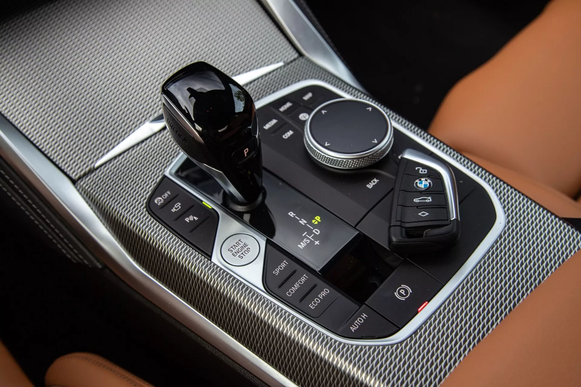 Gros plan sur la console centrale de la BMW Série 2 Coupé 2022, mettant en avant le levier de vitesse, le sélecteur de commande multimédia et le panneau de commande tactile avec finitions noir brillant et textures en fibre de carbone.
