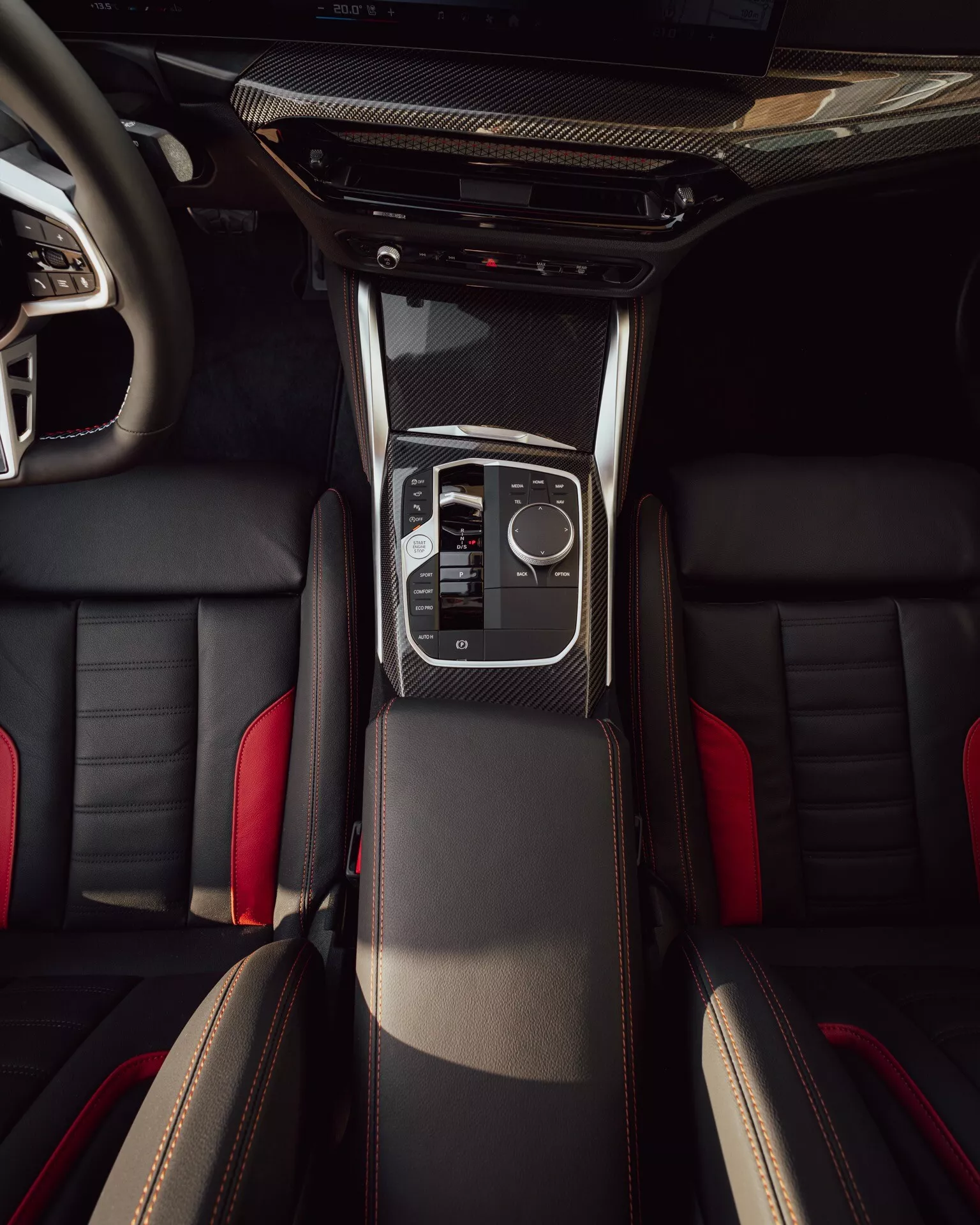 Vue intérieure en surplomb de la BMW Série 2 2024 (facelift G42-G87) montrant la console centrale avec garniture en fibre de carbone, élégant levier de vitesses, pavé tactile électronique, commandes climatiques, sièges avant en cuir à surpiqûres contrastées, et vue partielle des sièges arrière.