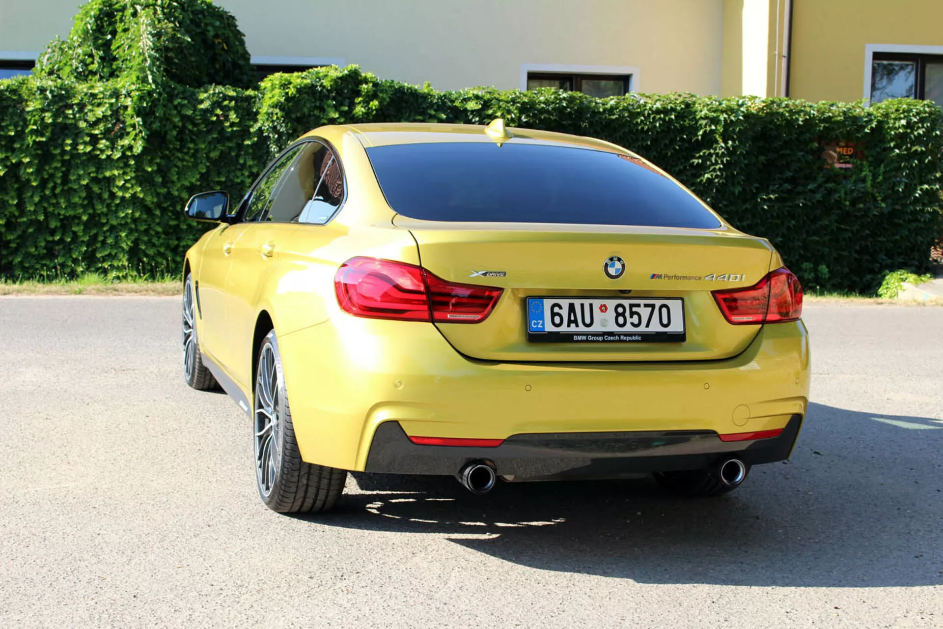 BMW Série 4 Coupé jaune de 2013 vue sous un angle arrière de trois quarts montrant la conception du coffre, le pare-choc arrière, une partie du passage de roue arrière, les feux arrière distinctifs, les tuyaux d'échappement doubles, la plaque d'immatriculation, le badge BMW, la désignation du modèle, les capteurs de stationnement, l'antenne aileron de requin, et les roues en alliage à multiples branches, stationnée dans un cadre urbain par une journée ensoleillée.
