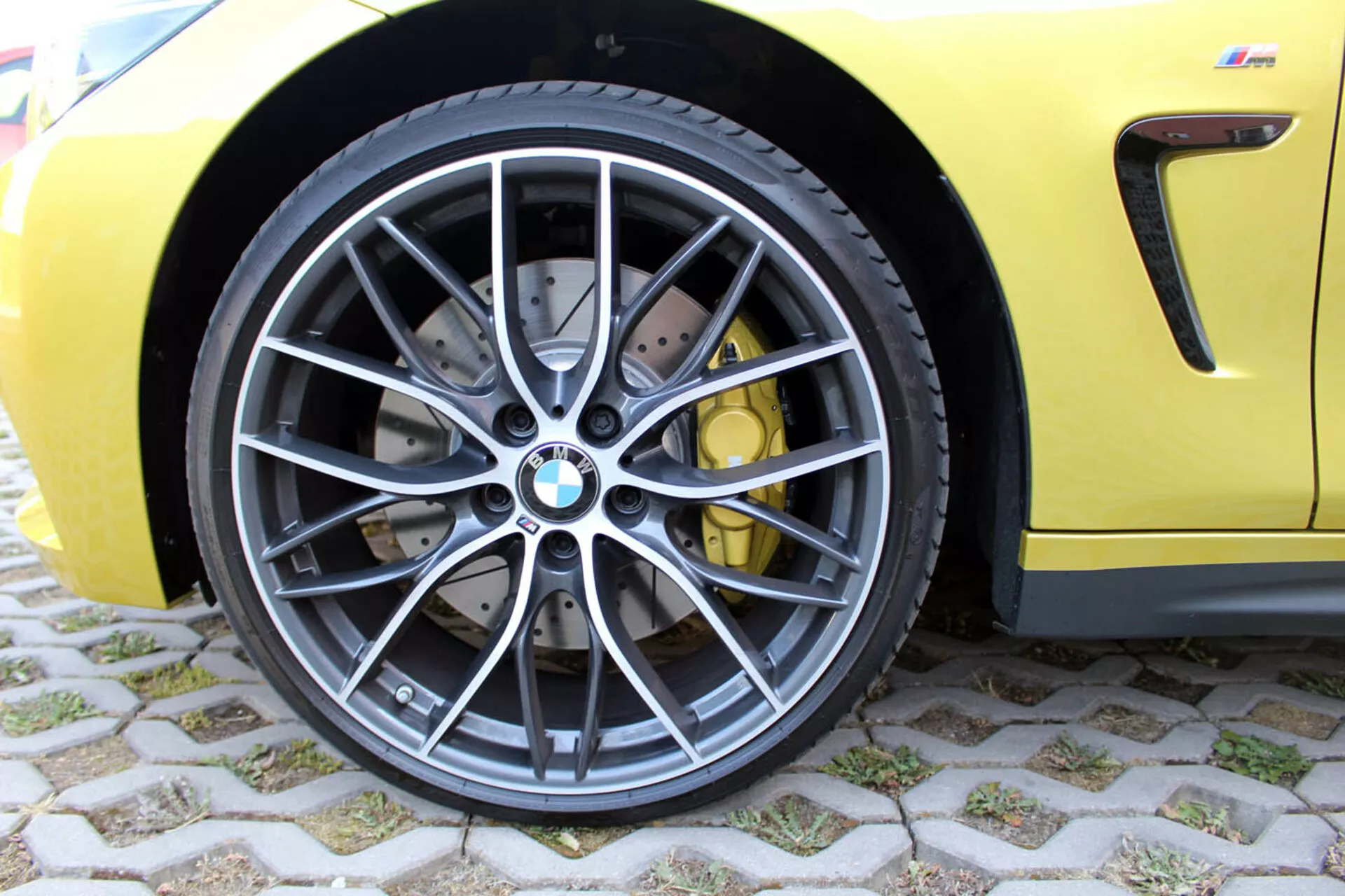 Vue rapprochée de la roue avant BMW Série 4 Coupé 2013 avec design à multiples rayons en alliage gris foncé, pneu radial sans chambre à air à profil bas, système de freinage haute performance avec disques percés et étriers jaunes, sur une carrosserie jaune sportive