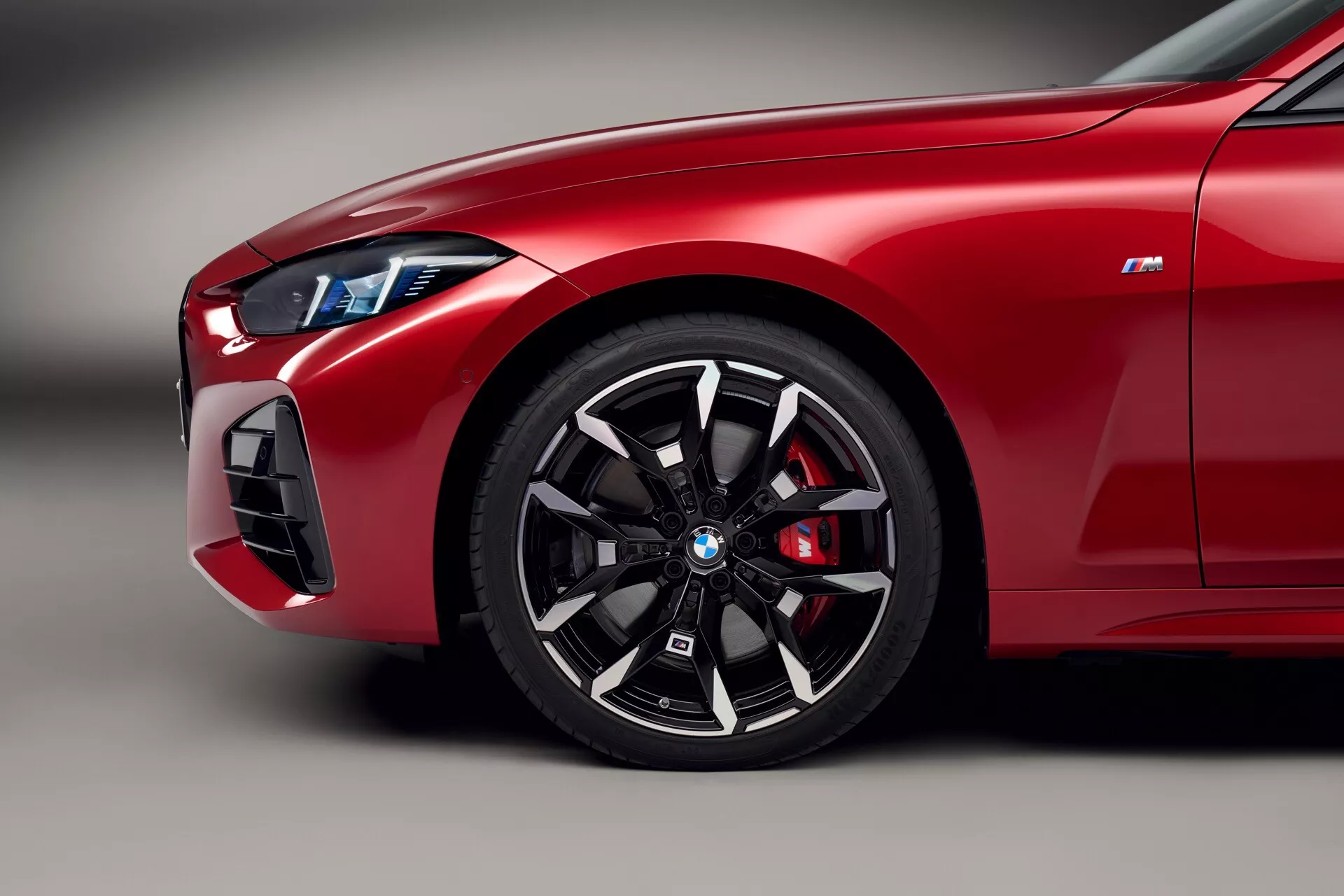 Image gros plan du quart avant rouge vif de la BMW Série 4 (G22-G23-G26-G82-G83 lifting) 2024, présentant une roue à multiples rayons, un étrier de frein haute performance, un phare LED élégant et un badge 'M' indiquant les caractéristiques de la série BMW M.