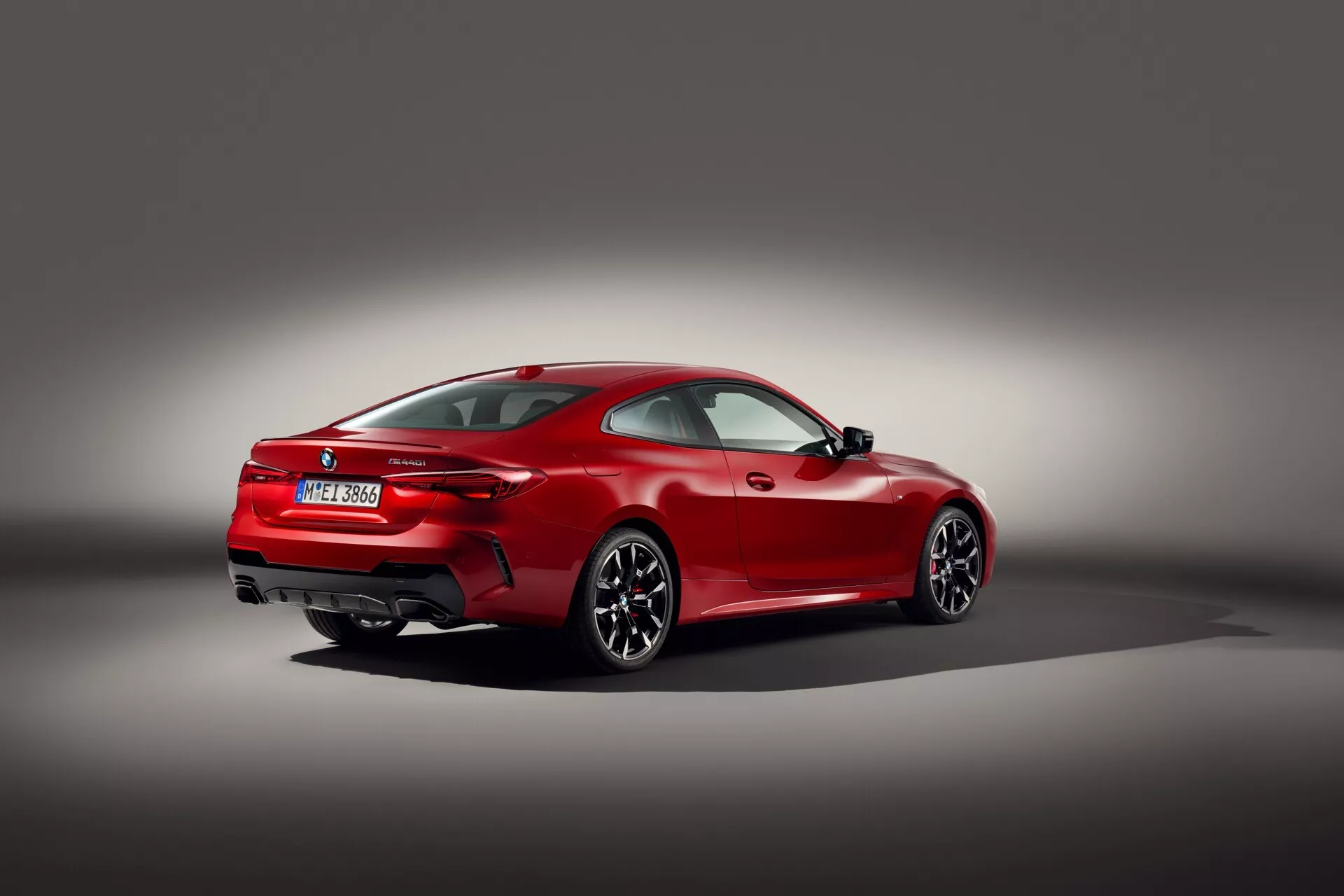 Coupé sportif rouge BMW Série 4 (G22-G23-G26-G82-G83 Facelift) de 2024 vu de trois quarts arrière contre un fond gris dégradé, montrant son design aérodynamique, son passage de roue arrière musclé, ses jantes alliage à rayons multiples, ses feux arrière horizontaux fins, ses embouts d'échappement doubles, son becquet arrière intégré et sa technologie LED sur des pneus performants à profil bas, reflétant un accent sur le luxe et la haute performance.