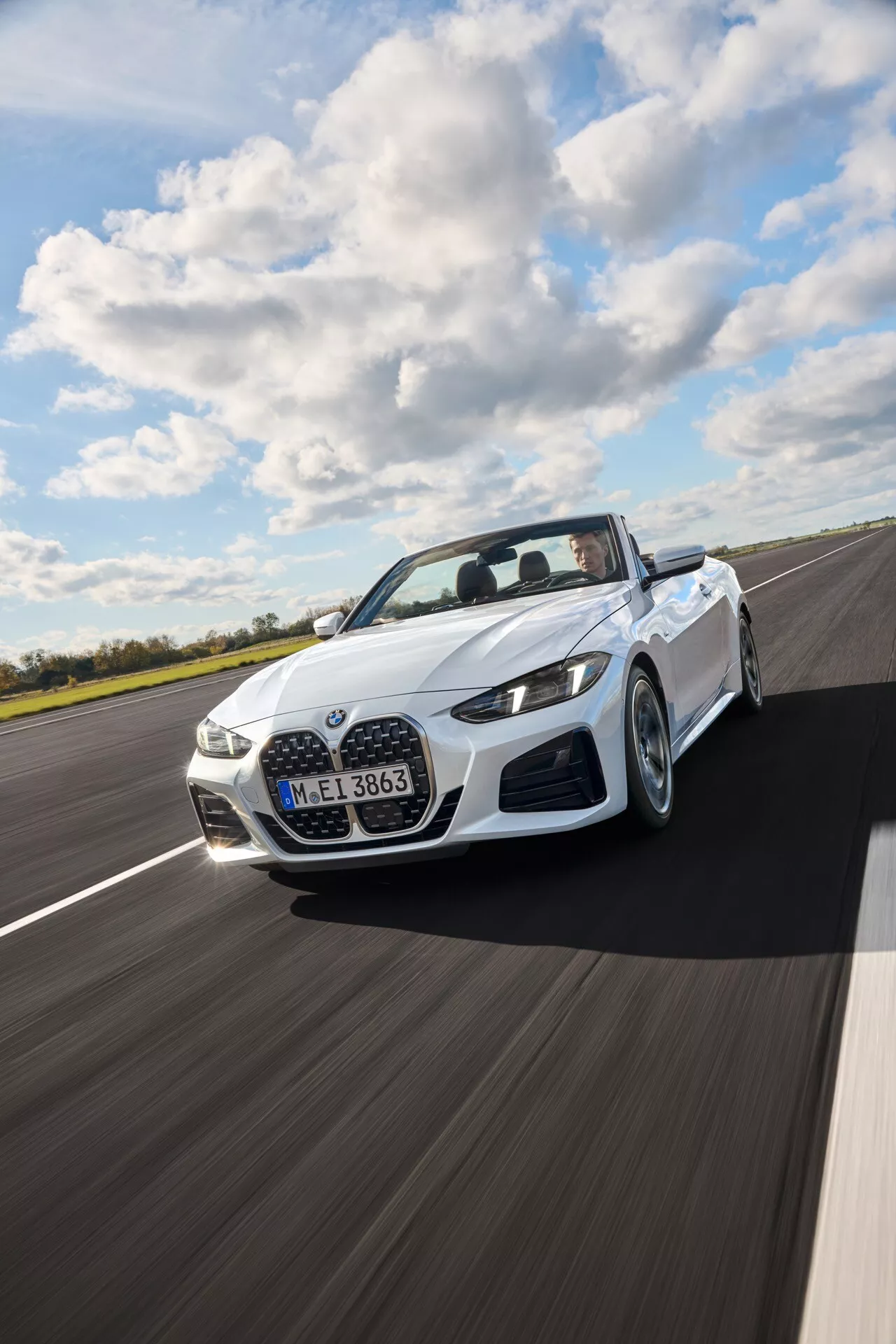 BMW Série 4 Cabriolet (G22-G23-G26-G82-G83 Facelift) de 2024 en blanc, roulant sur une route en asphalte sec sous un ciel partiellement nuageux, présentant une vue dynamique en trois quarts