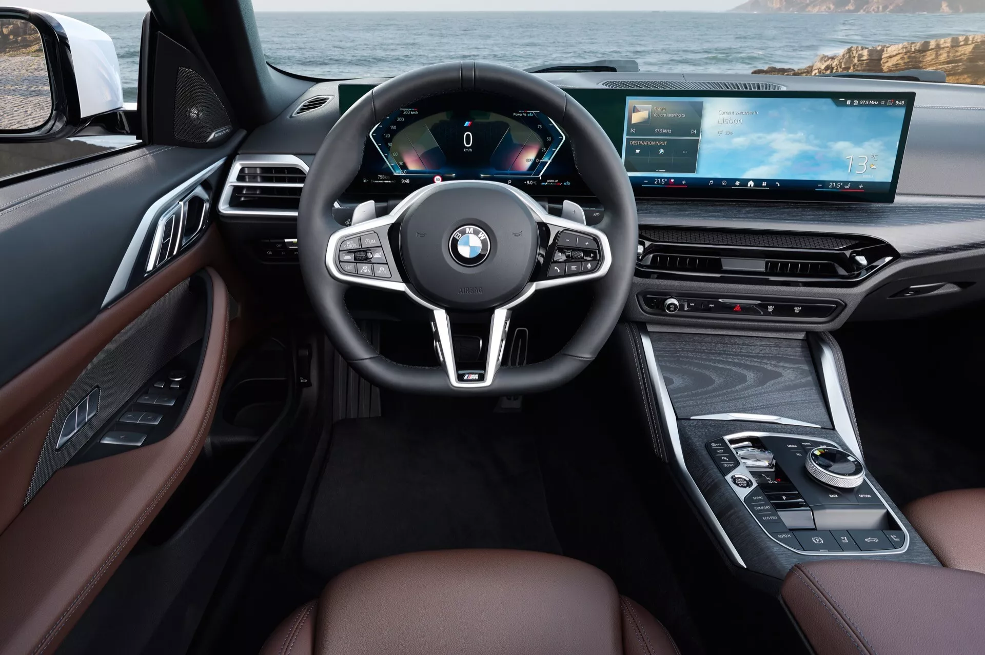 Vue intérieure de la BMW Série 4 2024 (G22-G23-G26-G82-G83-facelift) du point de vue du conducteur avec volant en cuir à trois branches, tableau de bord entièrement numérique, console centrale multimédia avancée avec écran tactile, sièges en cuir marron de luxe avec accents en bois et caractéristiques de design ergonomique moderne incluant des commandes multifonctions et un tableau de bord numérique