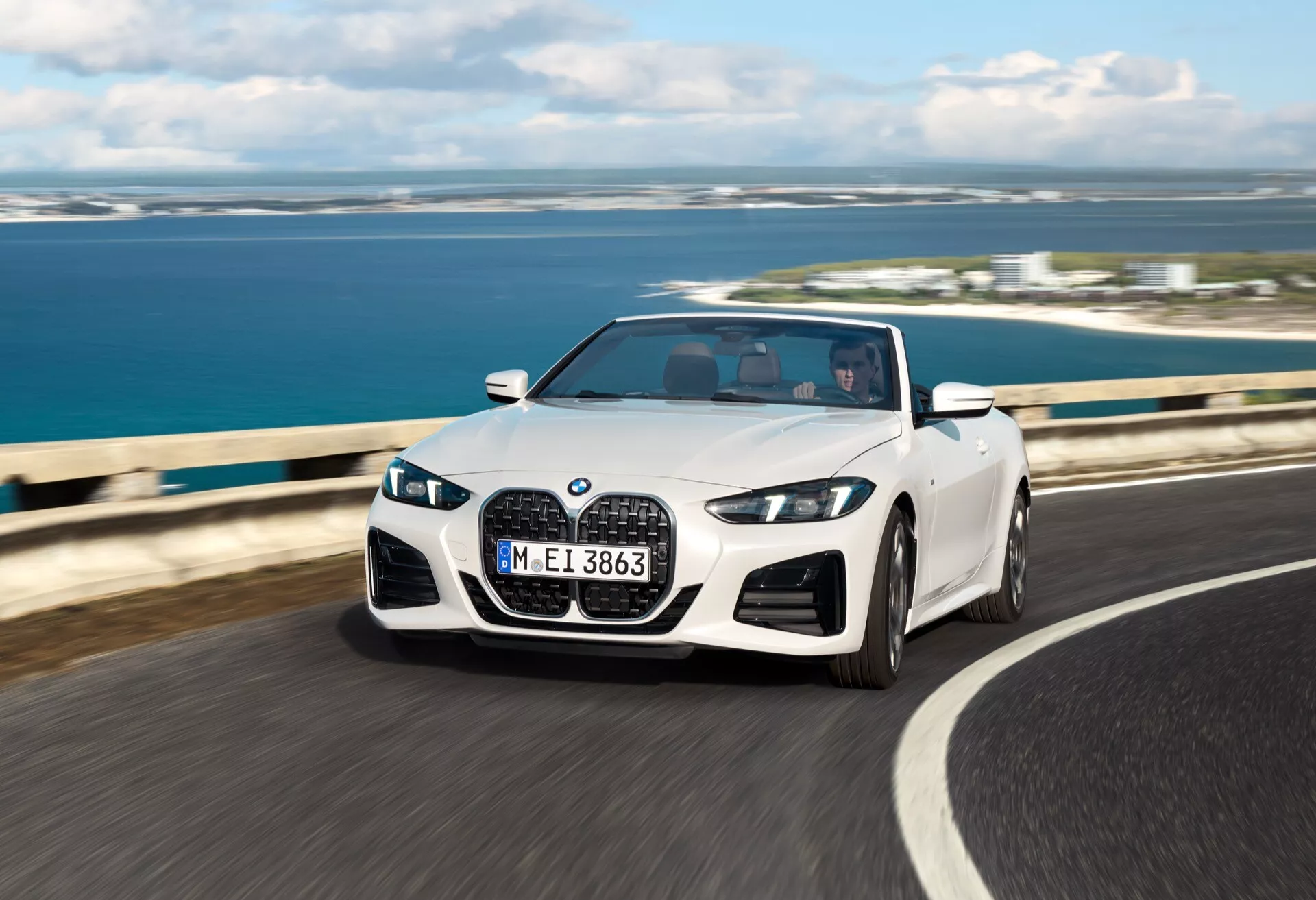 BMW Série 4 Cabriolet 2024 (G22-G23-G26-G82-G83 Facelift) en mouvement sur route côtière avec toit convertible baissé, phares LED, calandre à double rein et jantes en alliage sportives