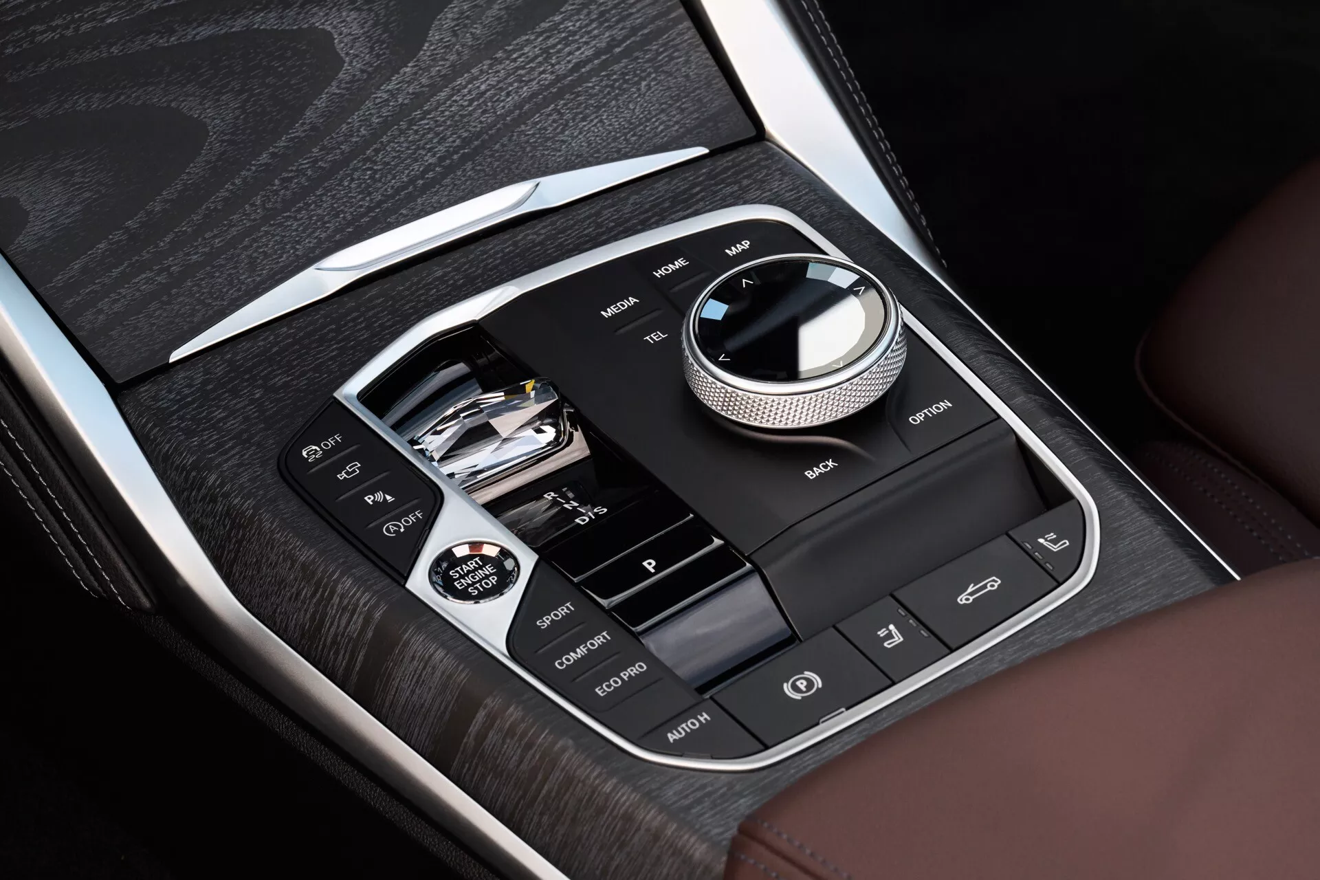 Vue rapprochée de la console centrale dans une BMW Série 4 2024 (G22-G23-G26-G82-G83 restylée) présentant les systèmes d'infodivertissement et de contrôle avec placage en bois et accents chromés, comportant une interface à molette circulaire principale, connectivité USB et emplacement pour carte SD, et boutons d'assistance au conducteur incluant le chauffage des sièges et ESC OFF