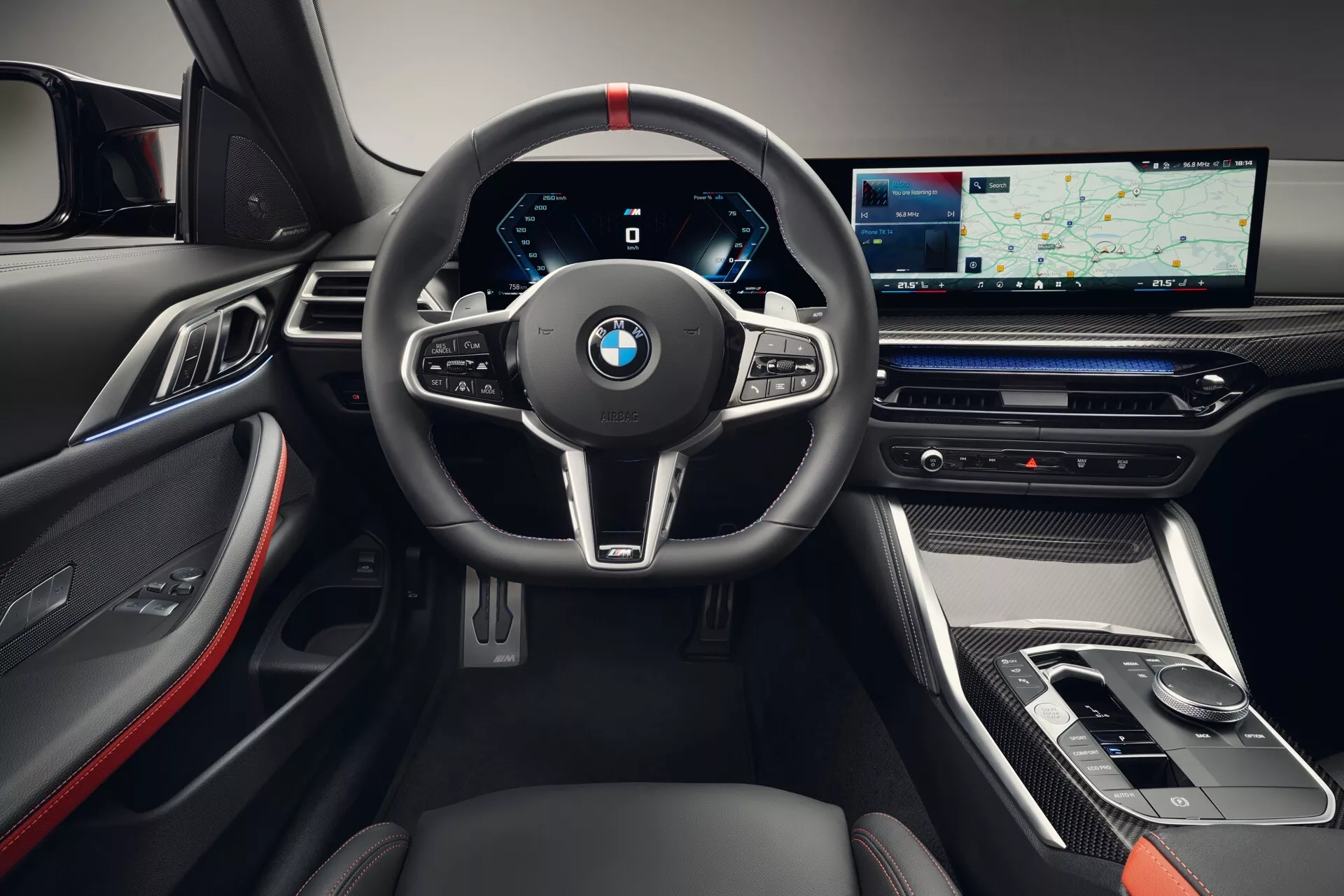 Vue intérieure de la BMW Série 4 2024 (G22-G23-G26-G82-G83 Facelift) mettant en avant le volant sportif à trois branches avec coutures rouges, tableau de bord entièrement numérique et console centrale élégante avec un grand écran tactile. Les détails révèlent des accents en fibre de carbone, des finitions luxueuses en cuir et métal, et une technologie infotainment avancée.