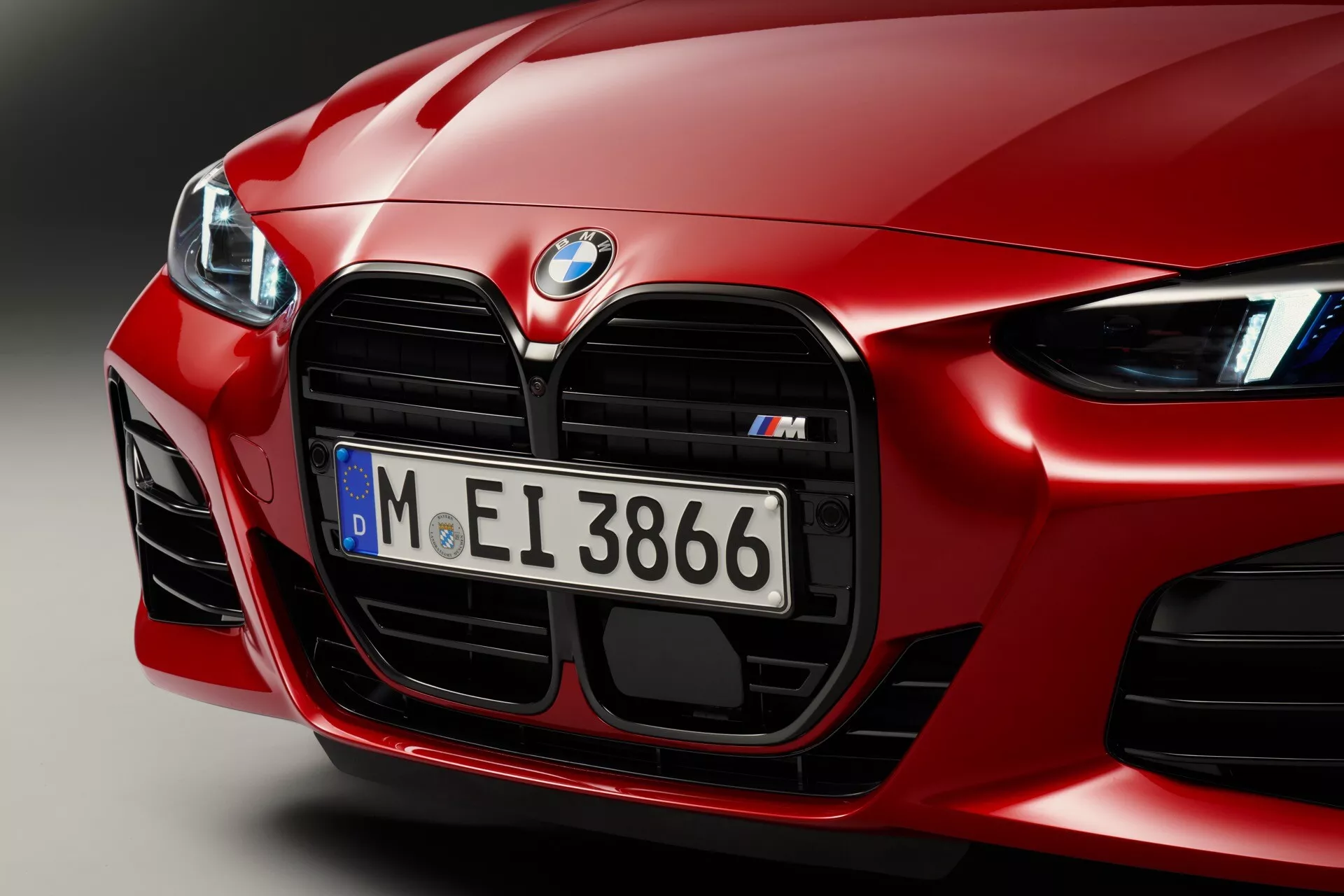 Gros plan sur l'avant d'une BMW Série 4 rouge 2024 (G22-G23-G26-G82-G83 Facelift), mettant en évidence son design aérodynamique, sa grille rénale de série M proéminente avec détails chromés, ses grandes entrées d'air orientées performance et ses phares LED de pointe